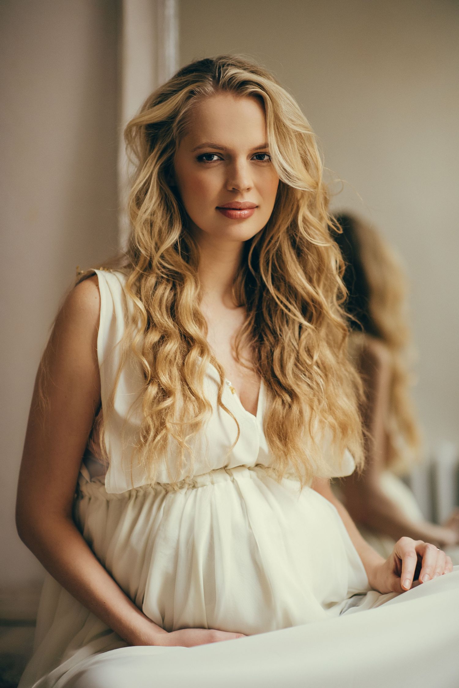 Elegant maternity portrait of woman in cream dress with flowing blonde hair.
