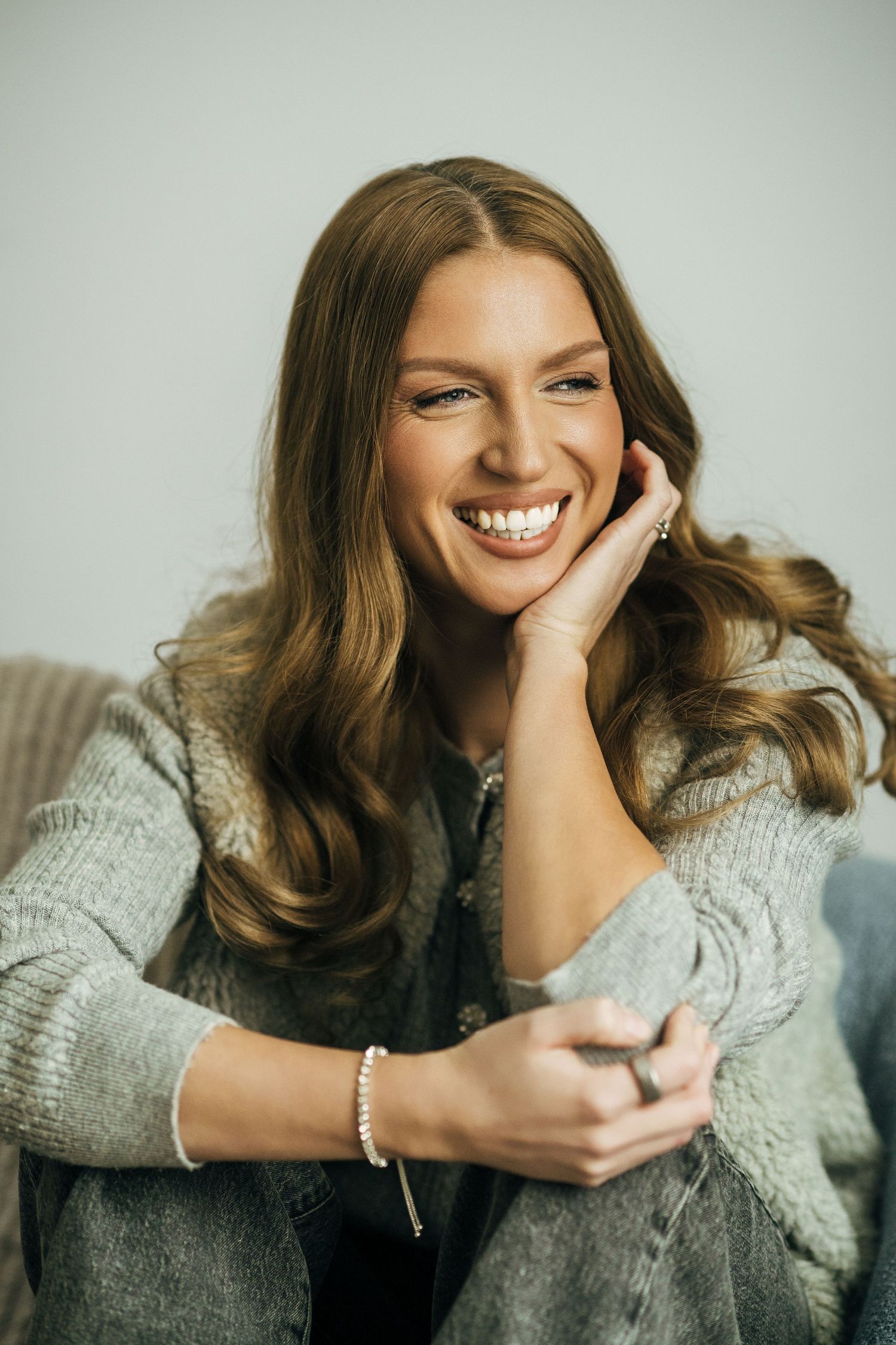 A person in a cozy gray sweater laughs while resting their head on their hand in a series of candid portraits.