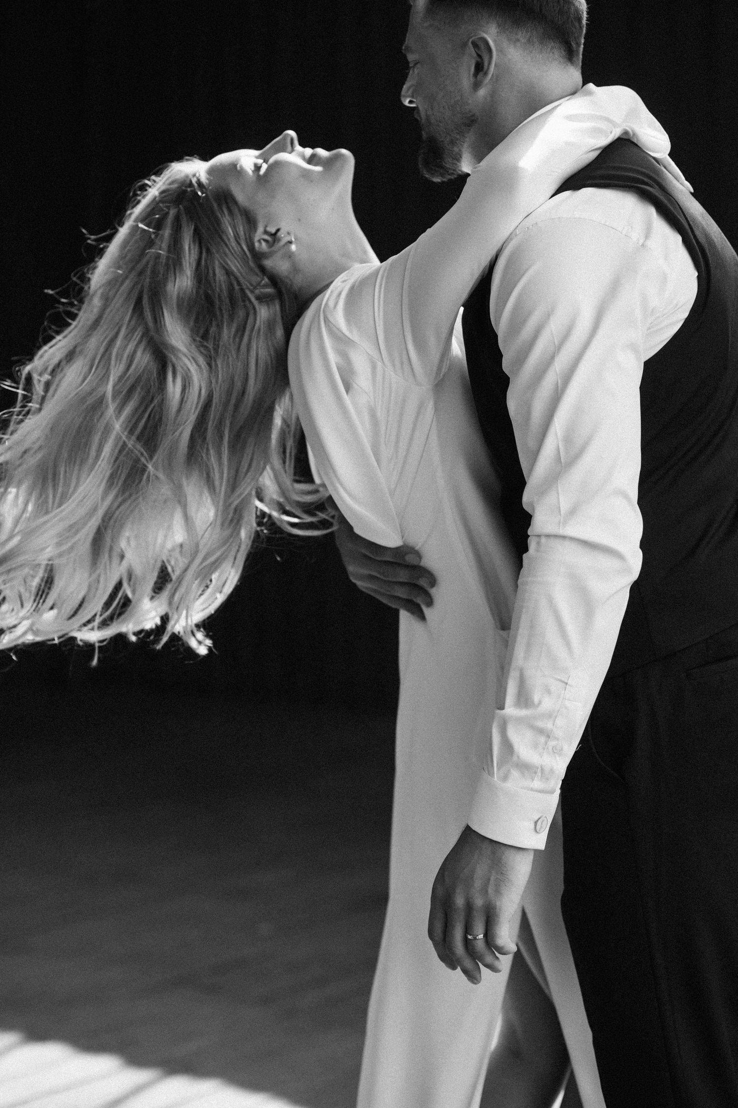 Black and white photo of a couple dancing romantically, woman in white dress leaning back gracefully, man in formal attire.