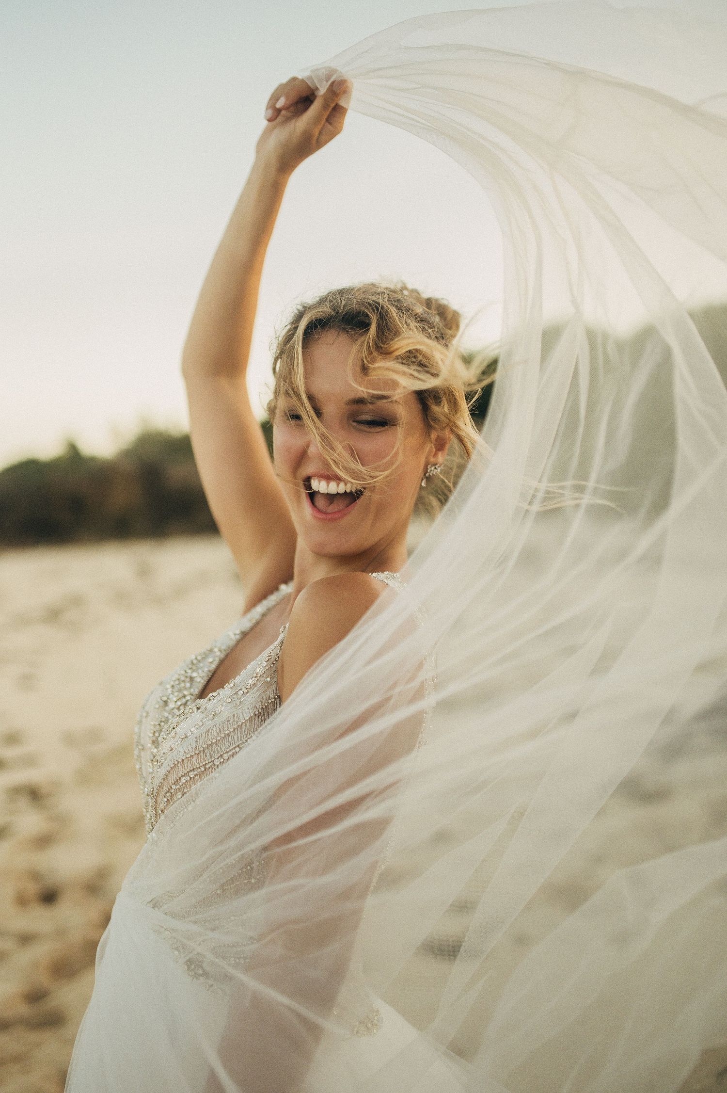 Flowing white wedding veil catches the sunlight as it billows in the ocean breeze.