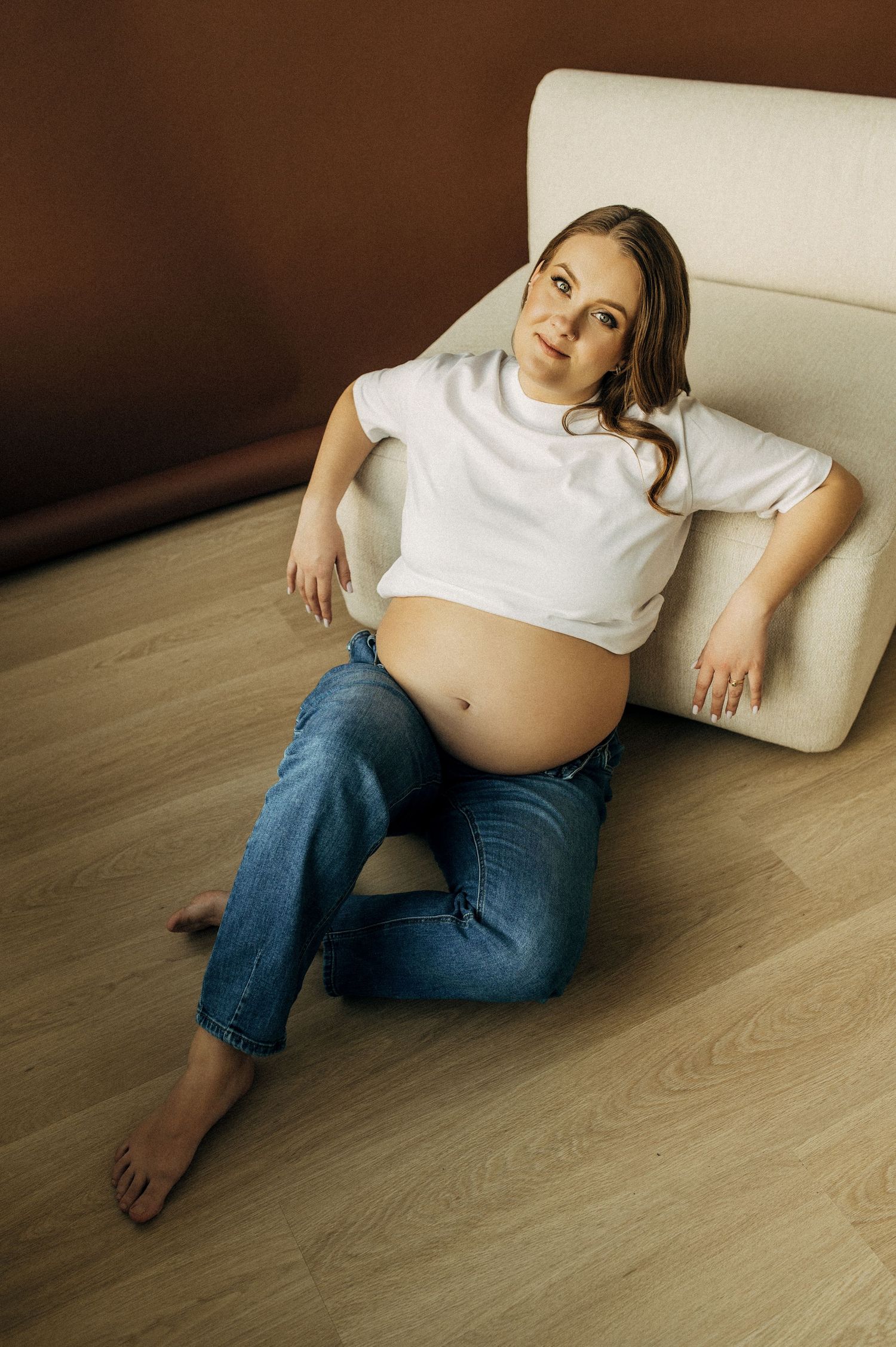 Casual maternity photos showing relaxed poses on light wooden flooring.