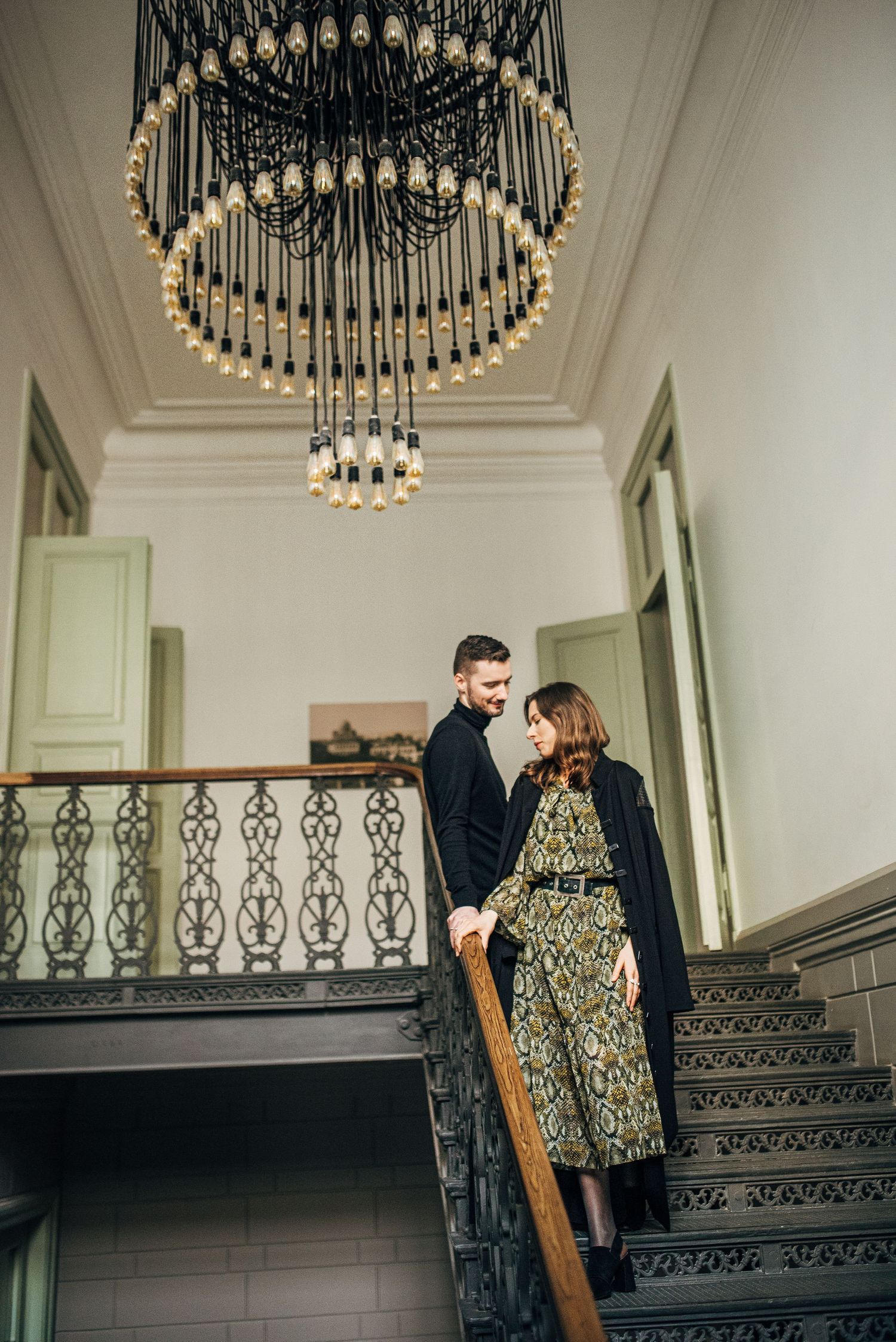 A romantic scene on ornate stairs under vintage chandeliers in an elegant interior.