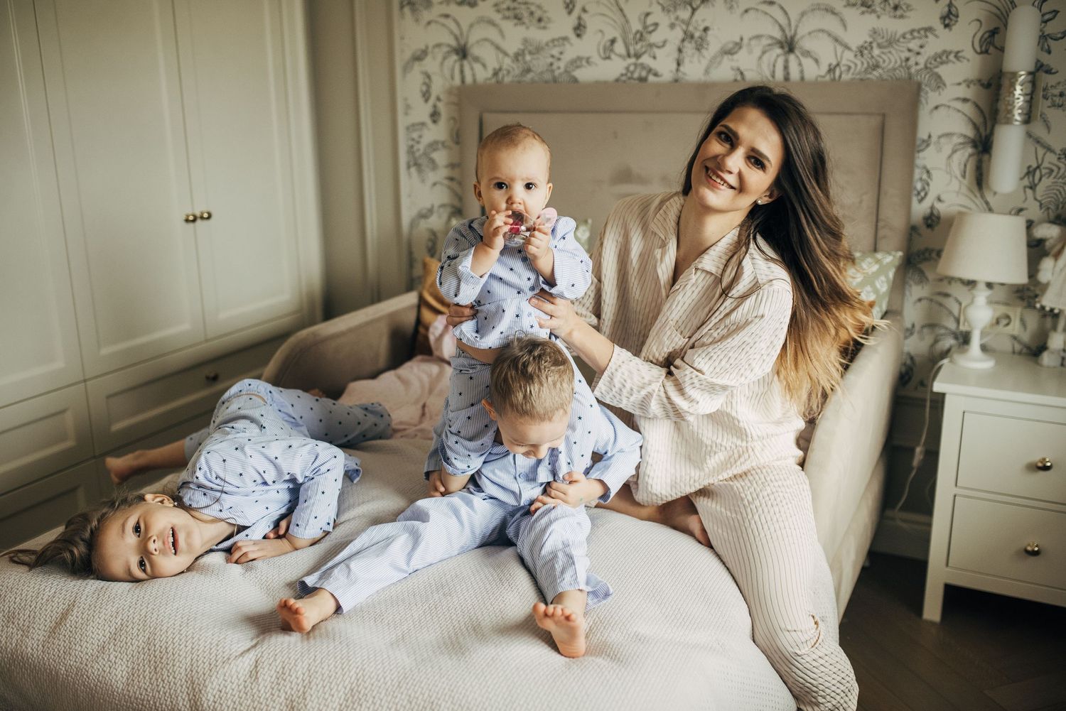 Intimate family moments captured in a bedroom with floral wallpaper.