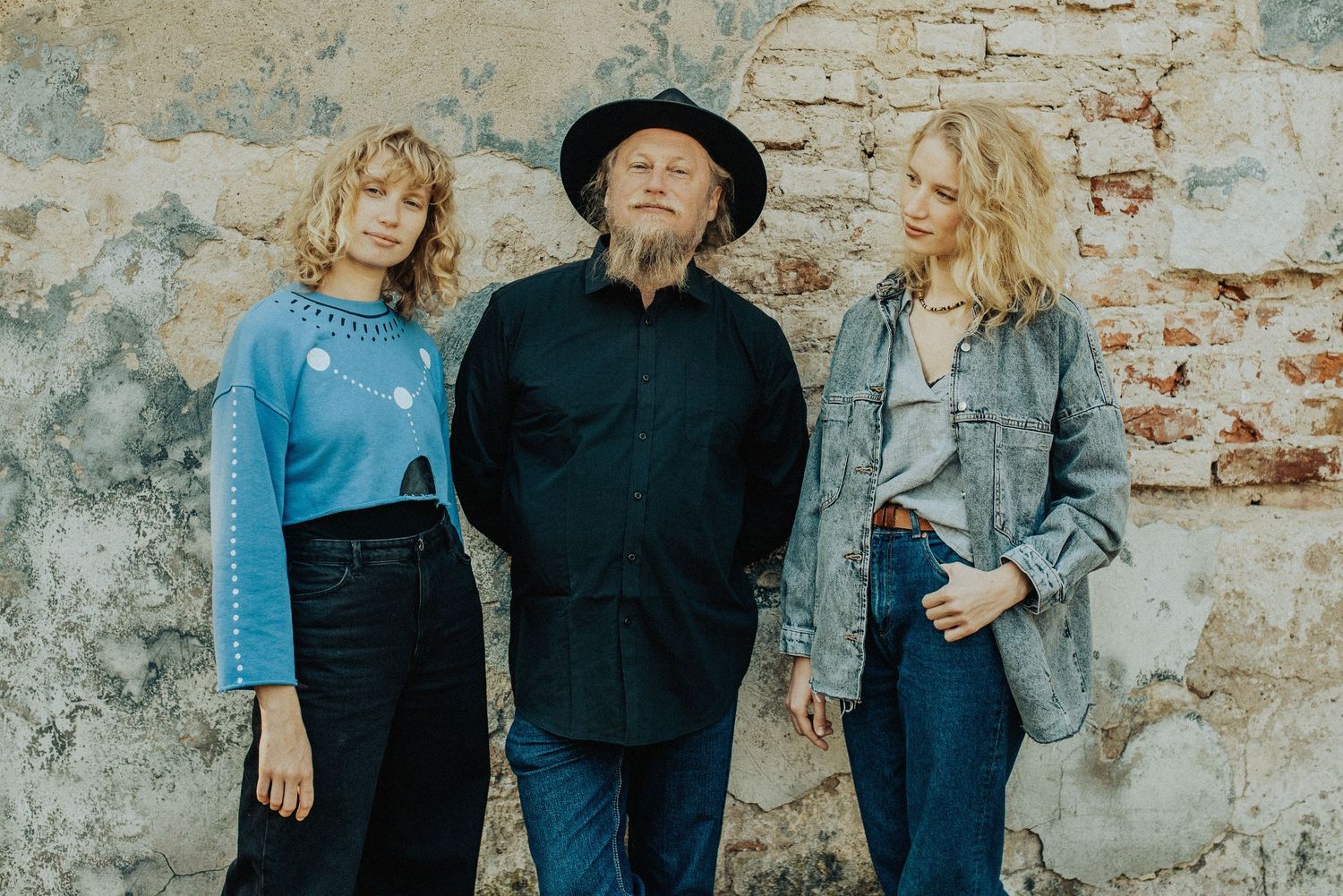 Group poses casually against rustic stone wall wearing coordinated blue and black outfits.
