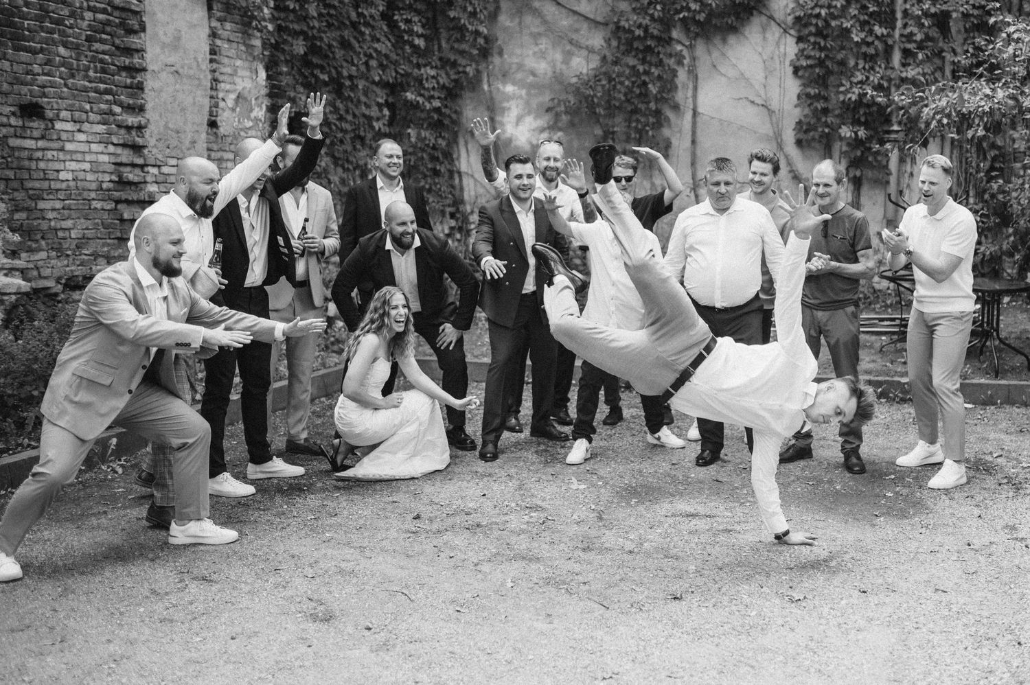 Black and white photo of wedding guests performing synchronized dance moves outdoors.