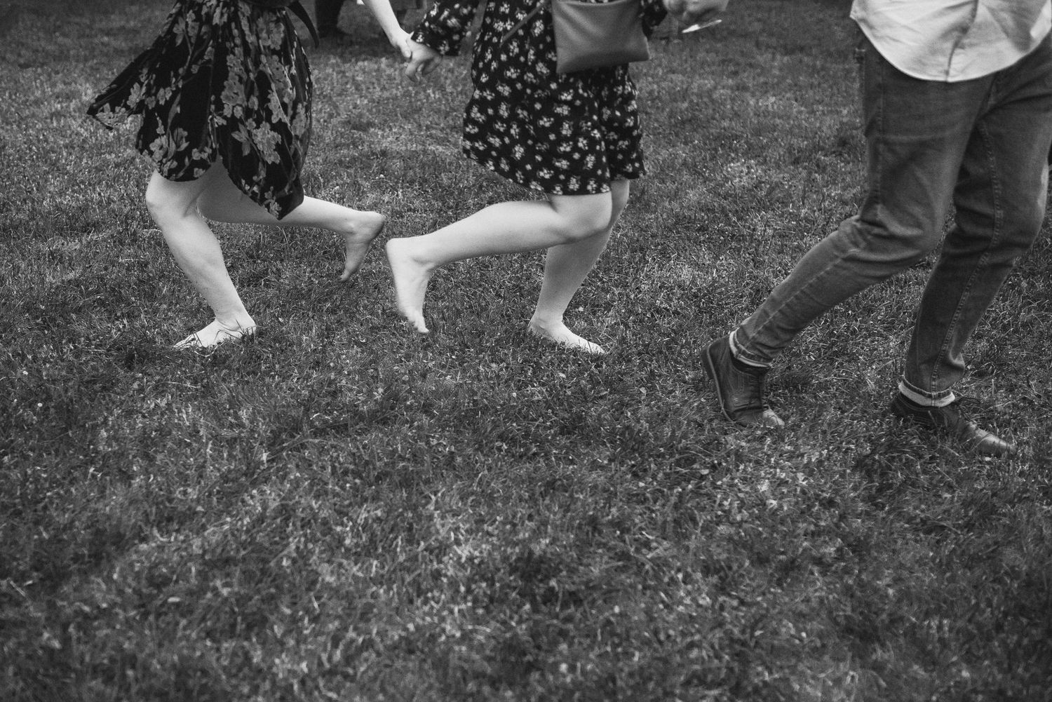 Black and white shot of feet dancing on grass at an outdoor event.