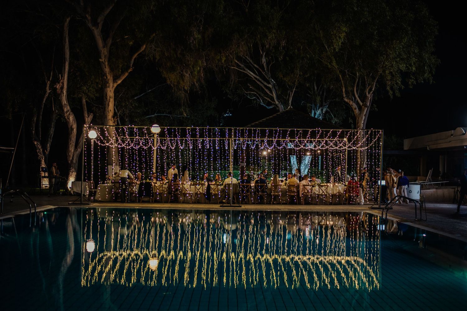 String lights reflect beautifully in a pool at an evening outdoor wedding reception.