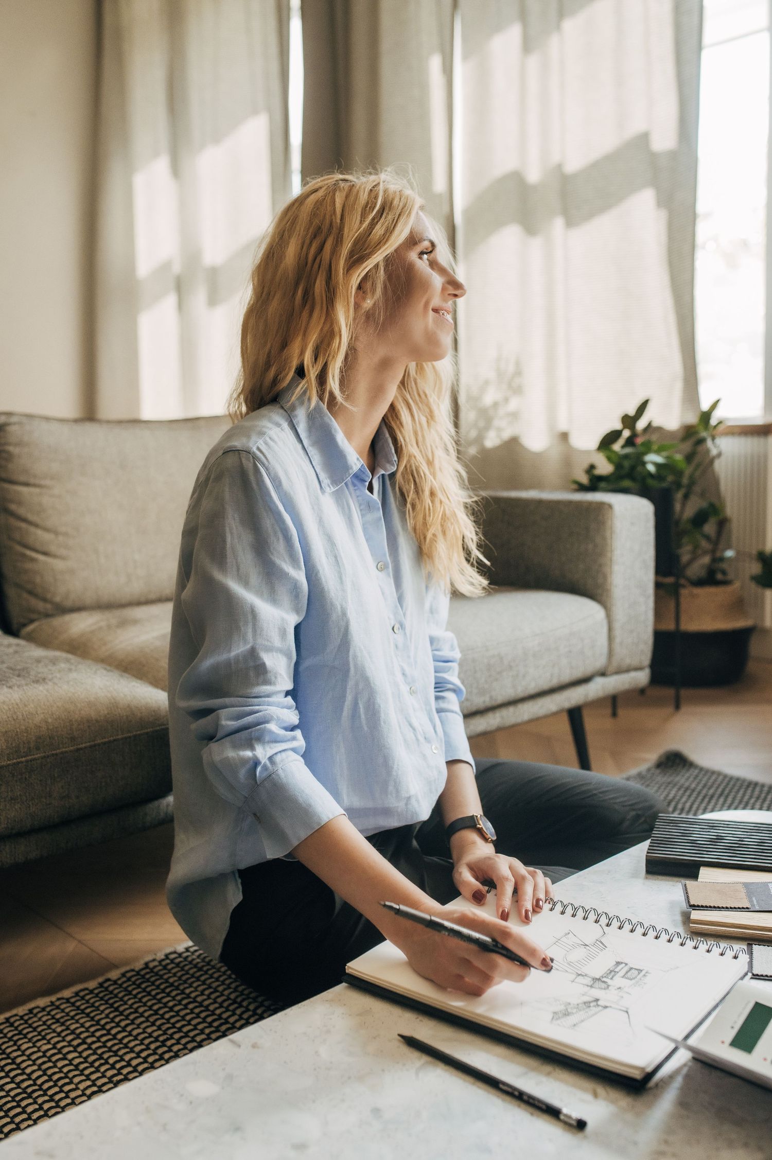 Person in light blue shirt working with notebooks and materials at a home desk.