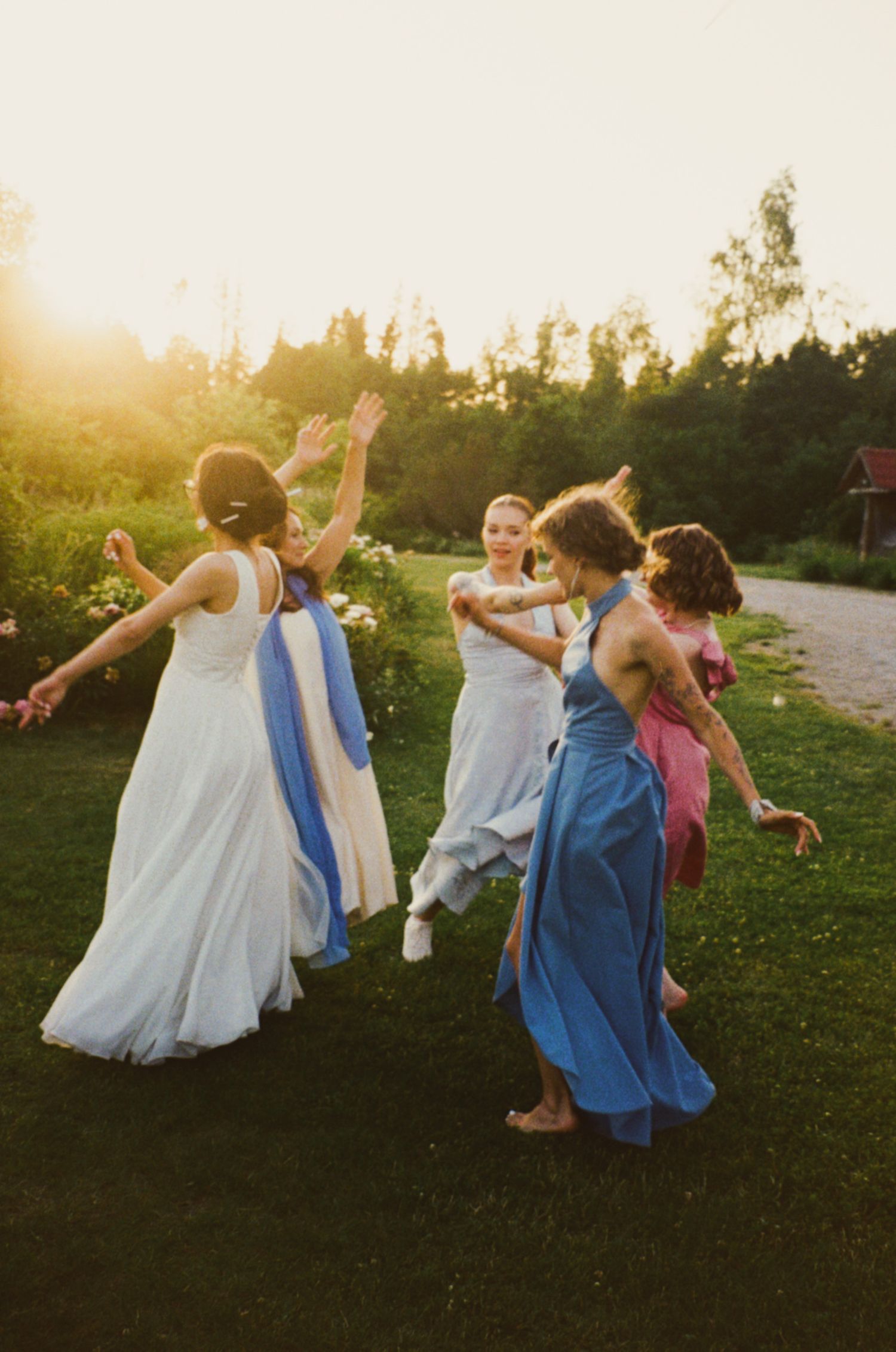 Women in elegant dresses dancing outdoors at golden hour during a summer wedding celebration.