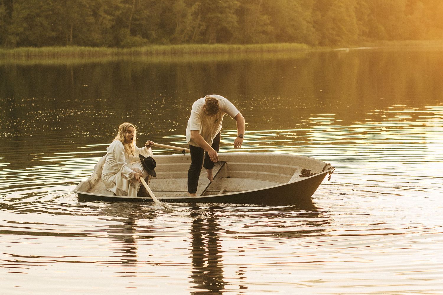 A paddleboard glides across a tranquil lake during golden hour, creating a serene reflection on the water's surface.