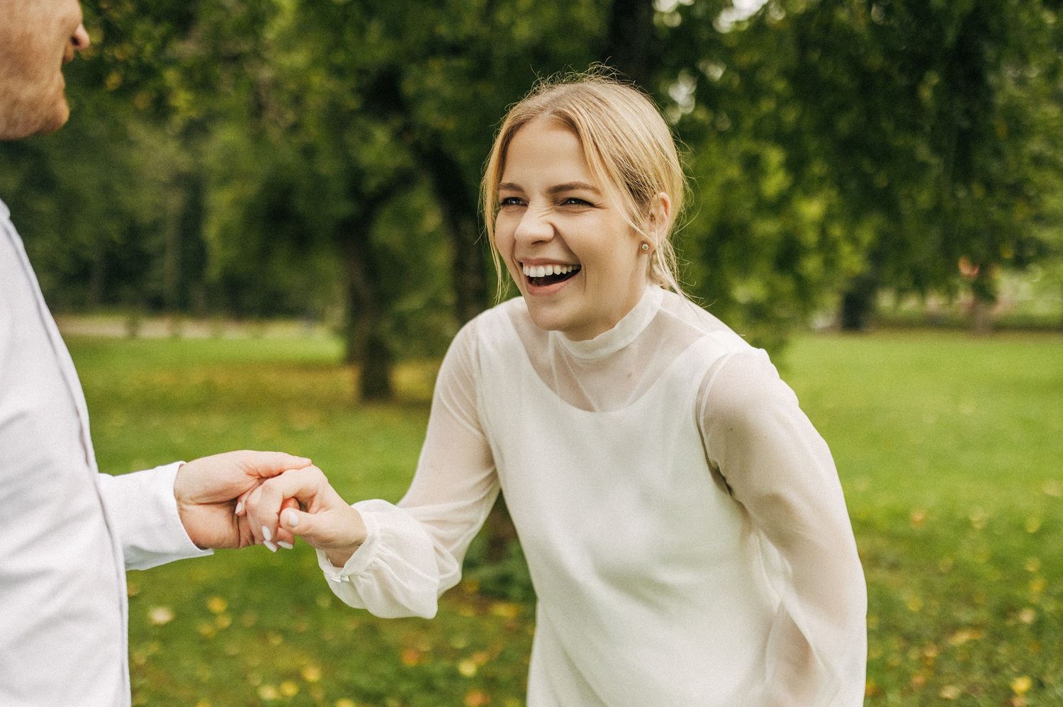 Wedding couple dancing and laughing together on grass in a sunlit garden setting.