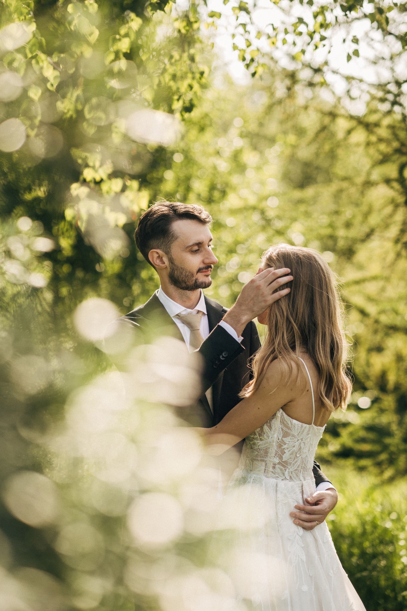 Newlyweds share intimate moment in sunlit garden with soft bokeh highlights.