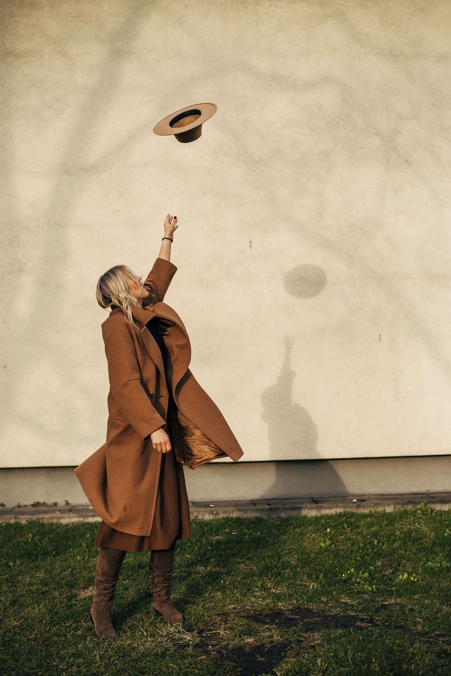Person in brown coat performing dynamic movements against white wall outdoors.