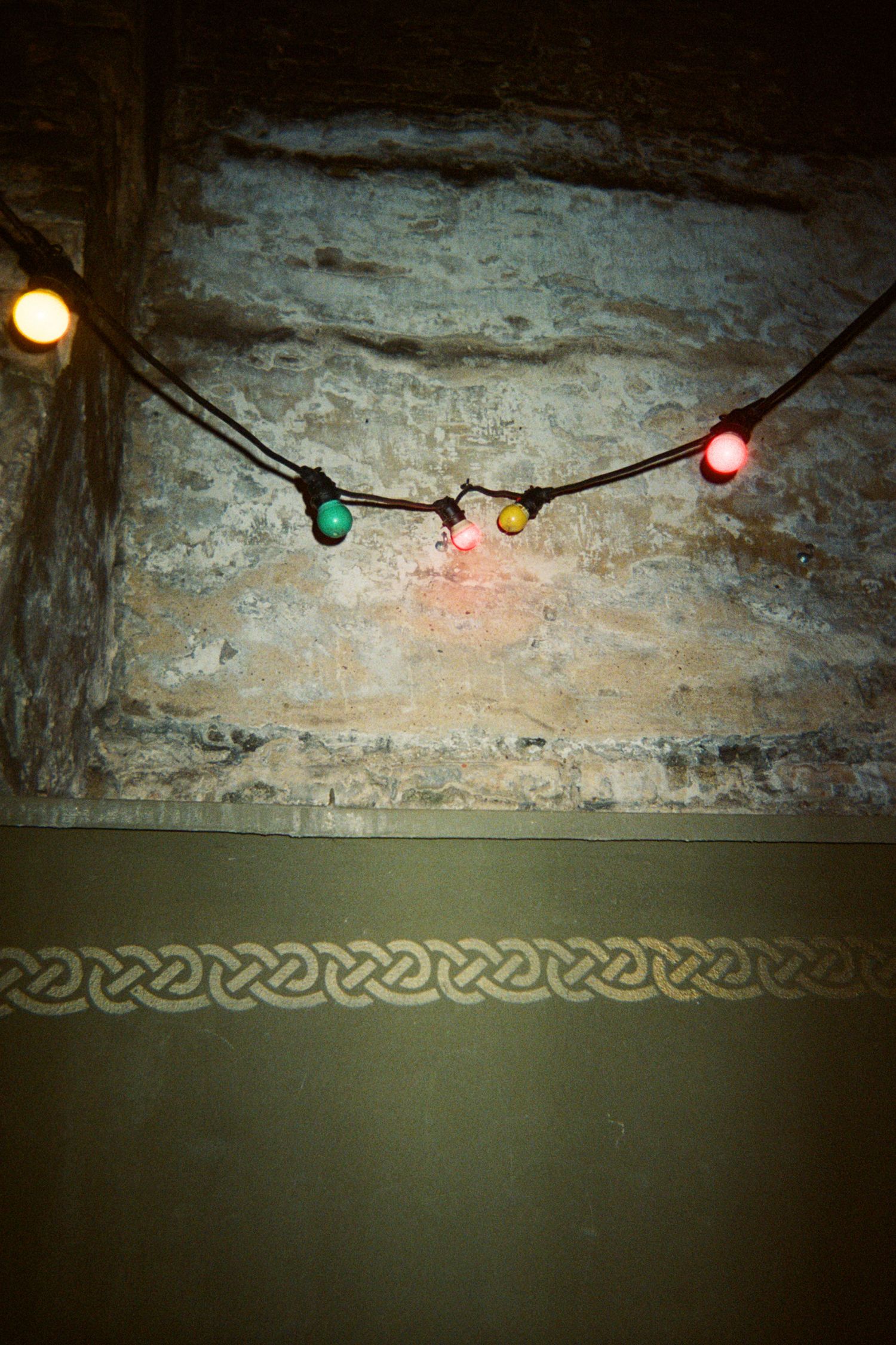 Vintage stone wall with decorative Celtic border pattern and colorful string lights creating moody ambiance.
