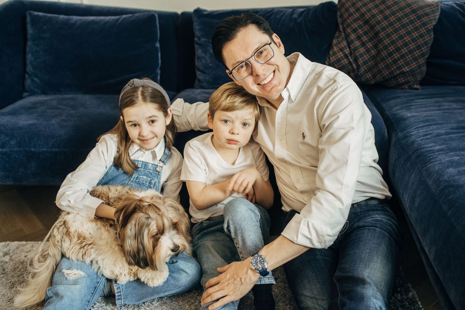 Family relaxing together with their small fluffy dog on a blue couch.