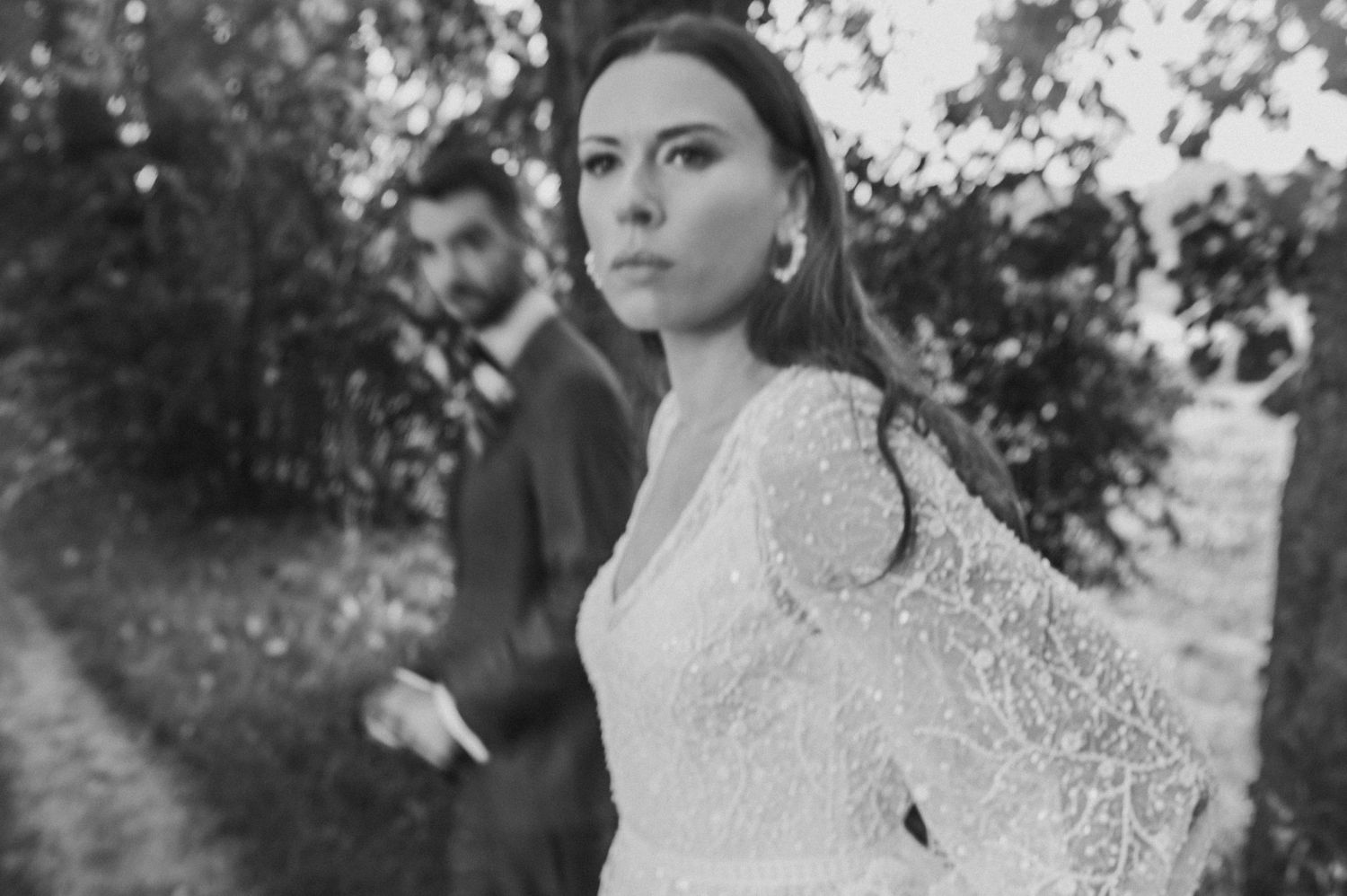 Bride in elegant lace wedding dress posing outdoors with natural lighting.