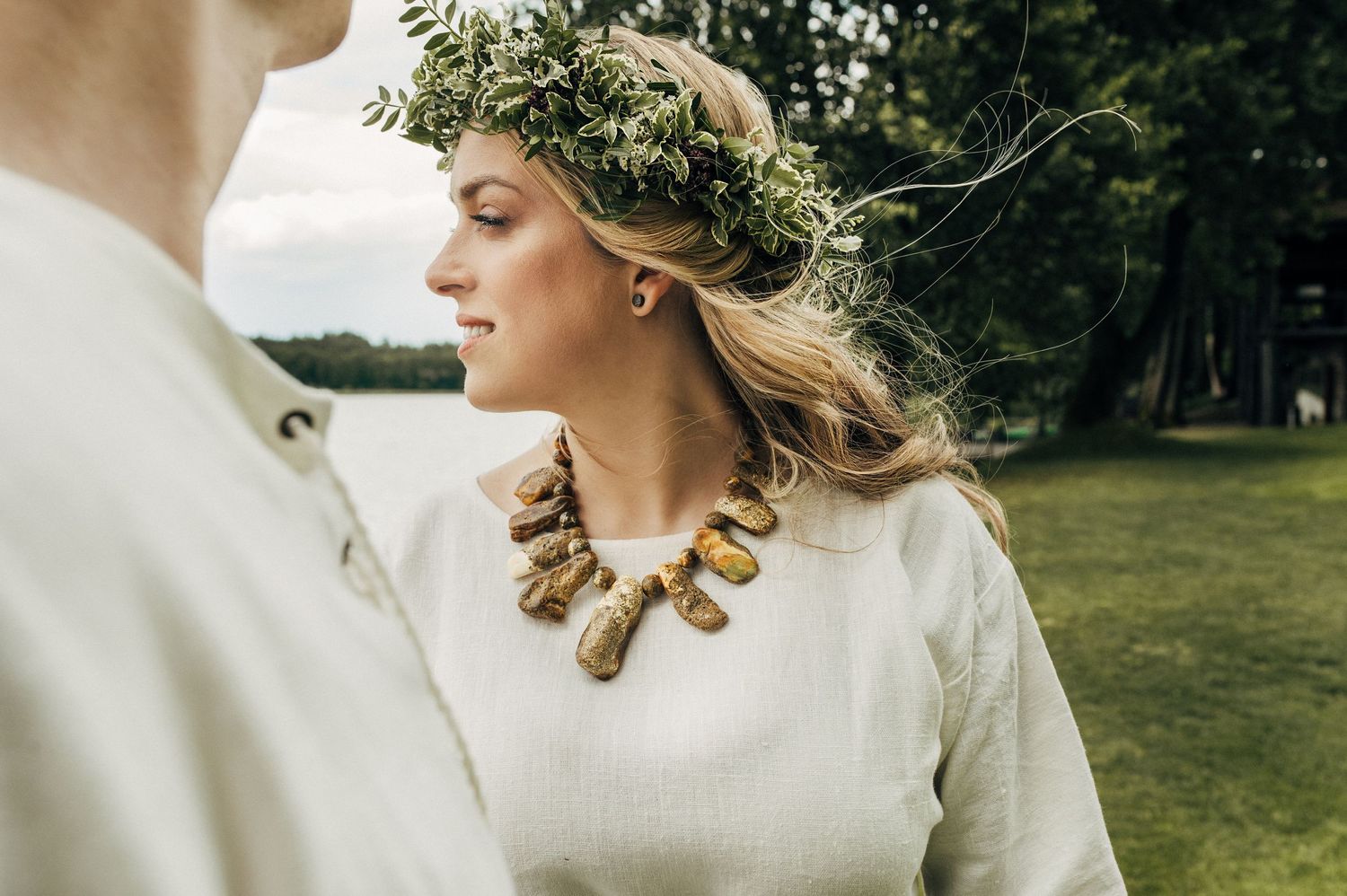 Wedding attire includes delicate flower crown and statement necklace in outdoor setting.