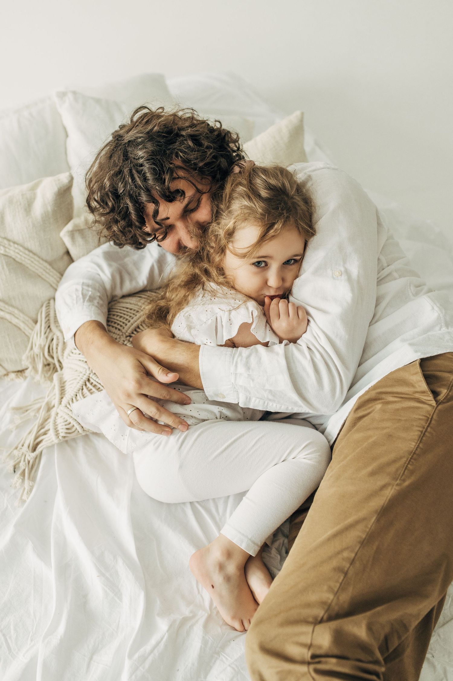 Intimate portrait of parent and child resting together on white bedding.