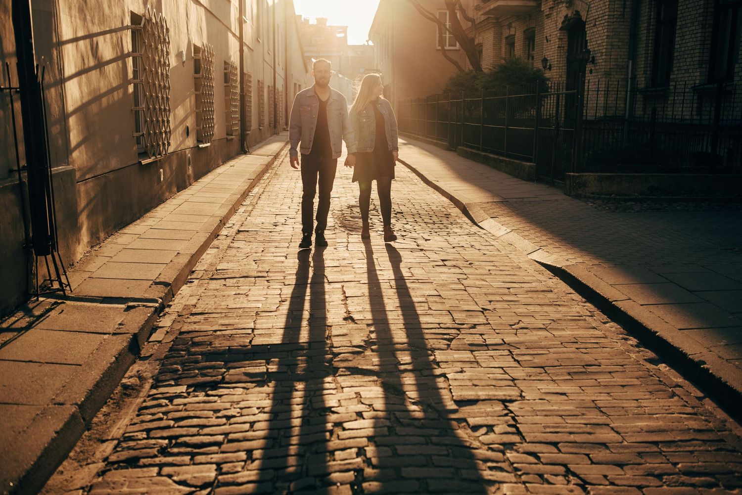 Silhouettes of people walking on cobblestone street at sunset.
