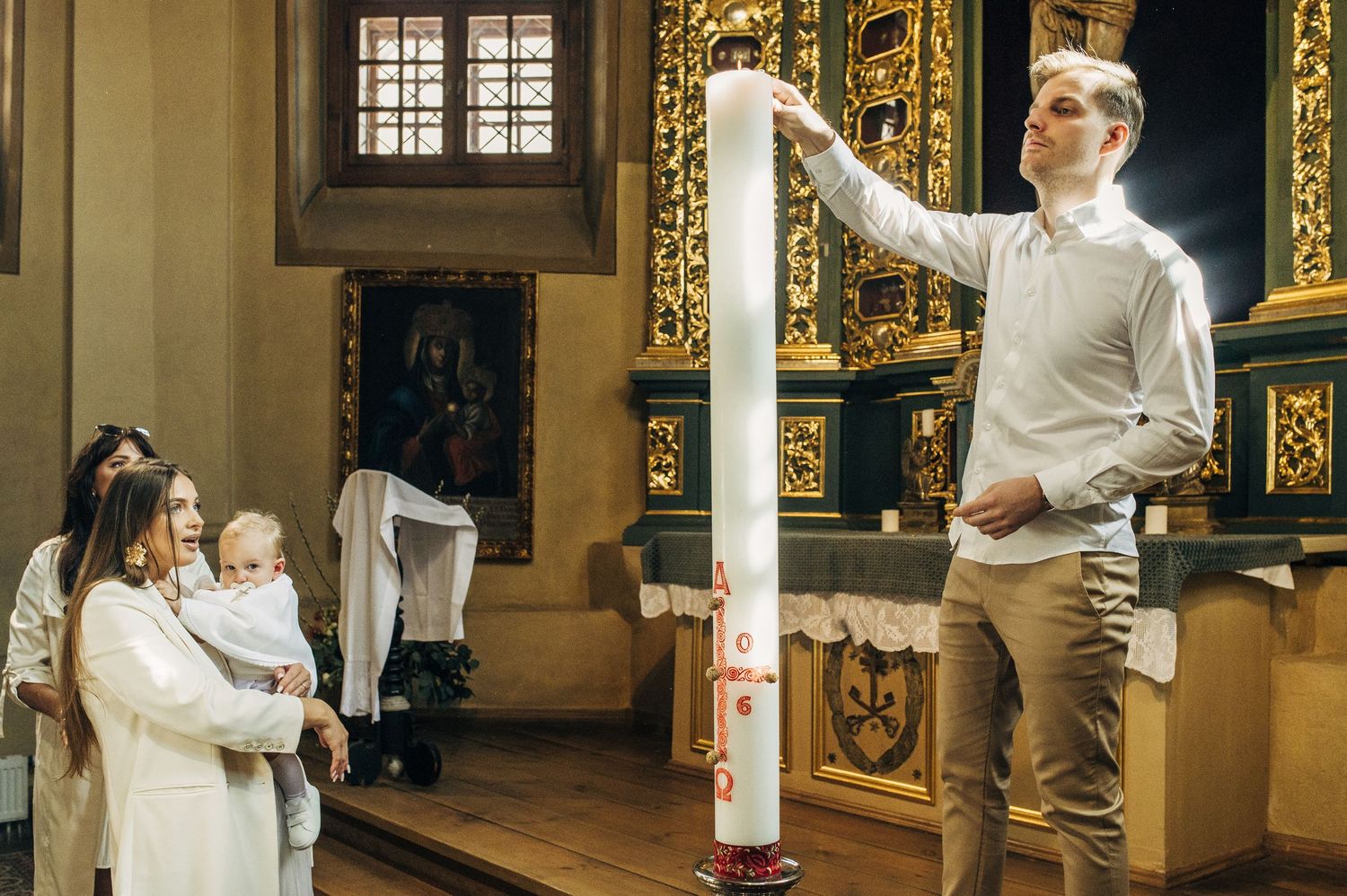 Man lighting a tall baptismal candle at a church christening ceremony.