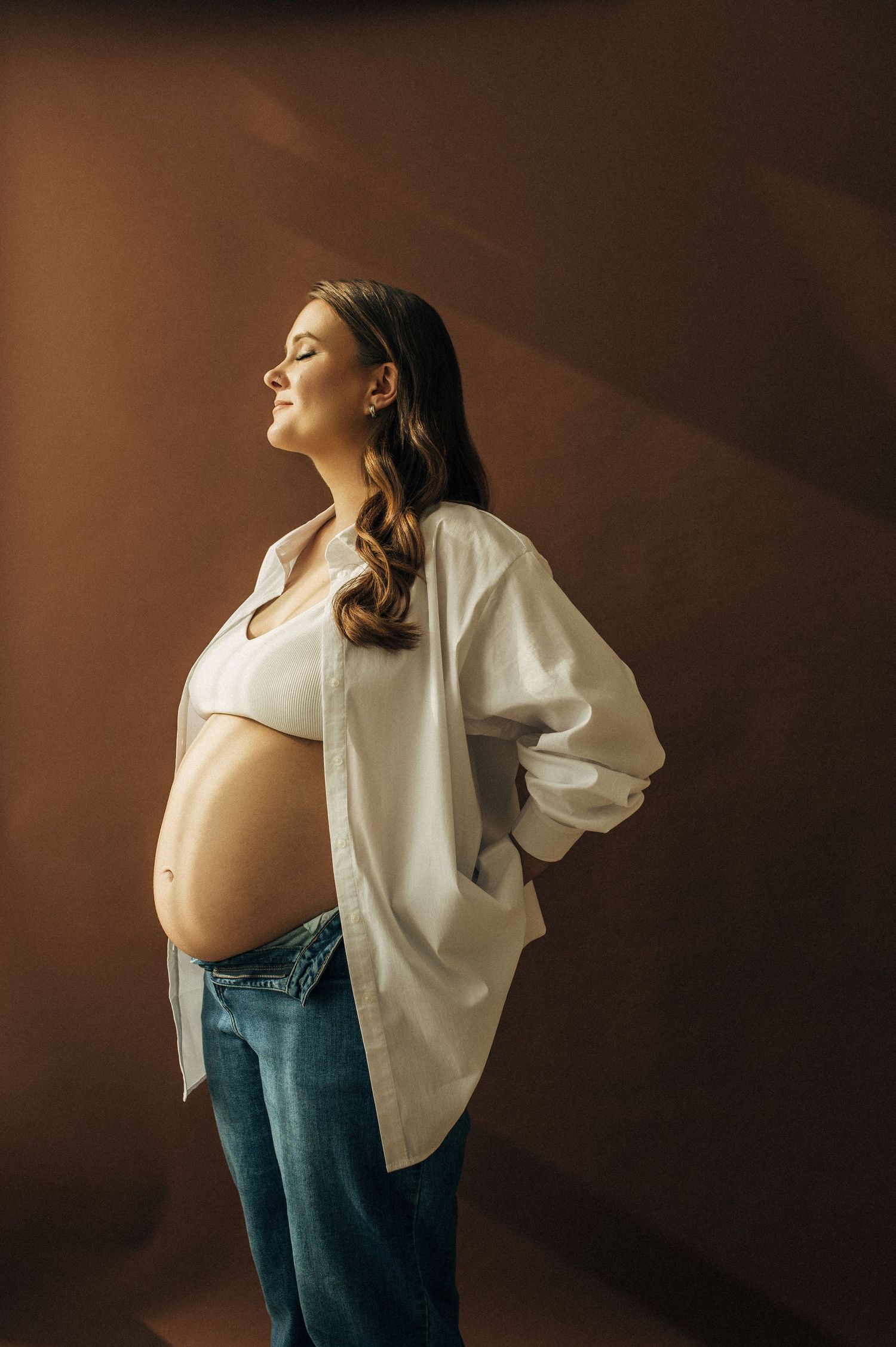 A maternity photoshoot featuring casual attire against a warm brown background.