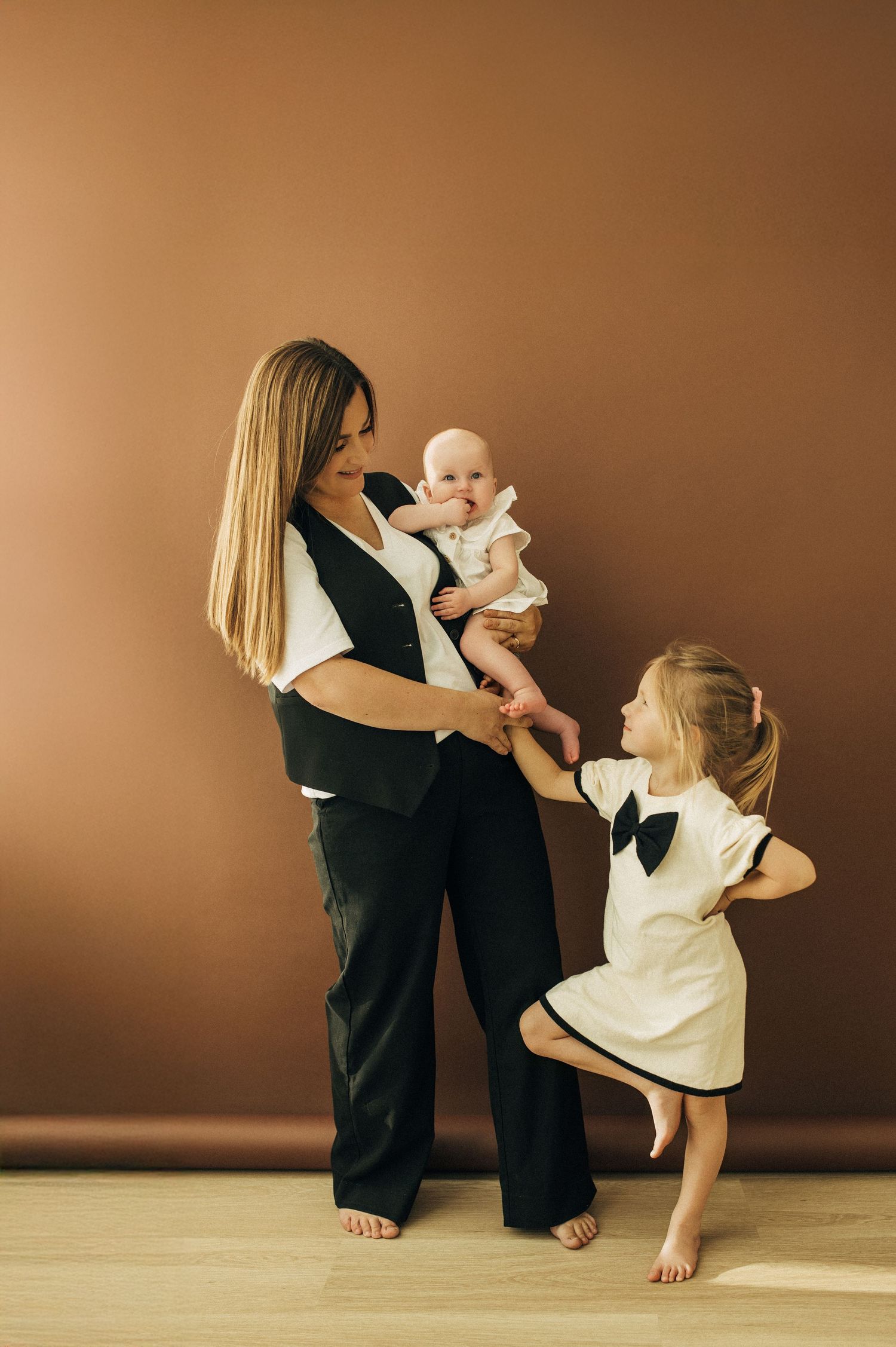 Artistic family portrait series in black and white outfits against warm brown backdrop.