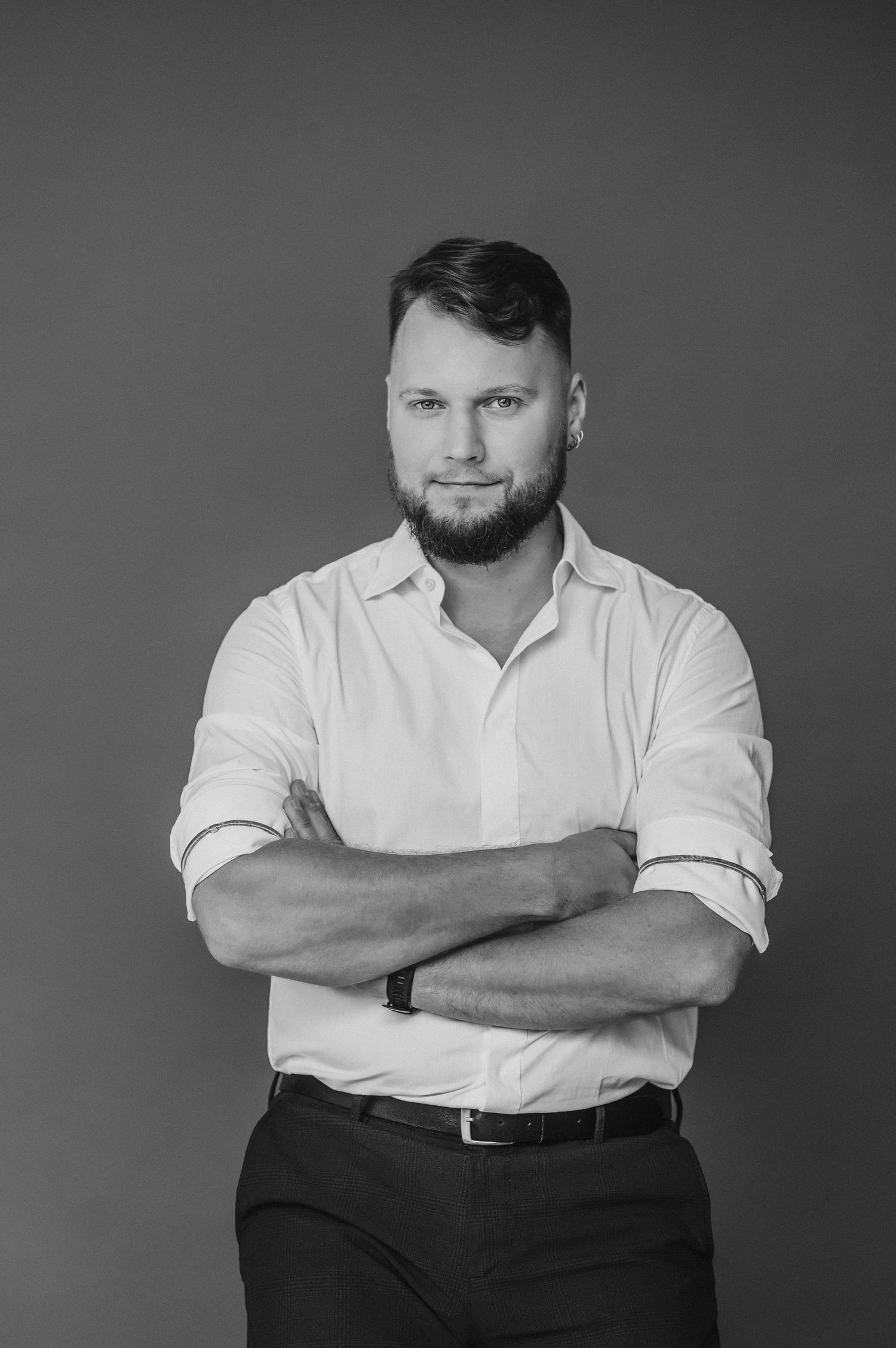 Monochrome portrait of a person wearing a white shirt and dark pants against a gray backdrop.