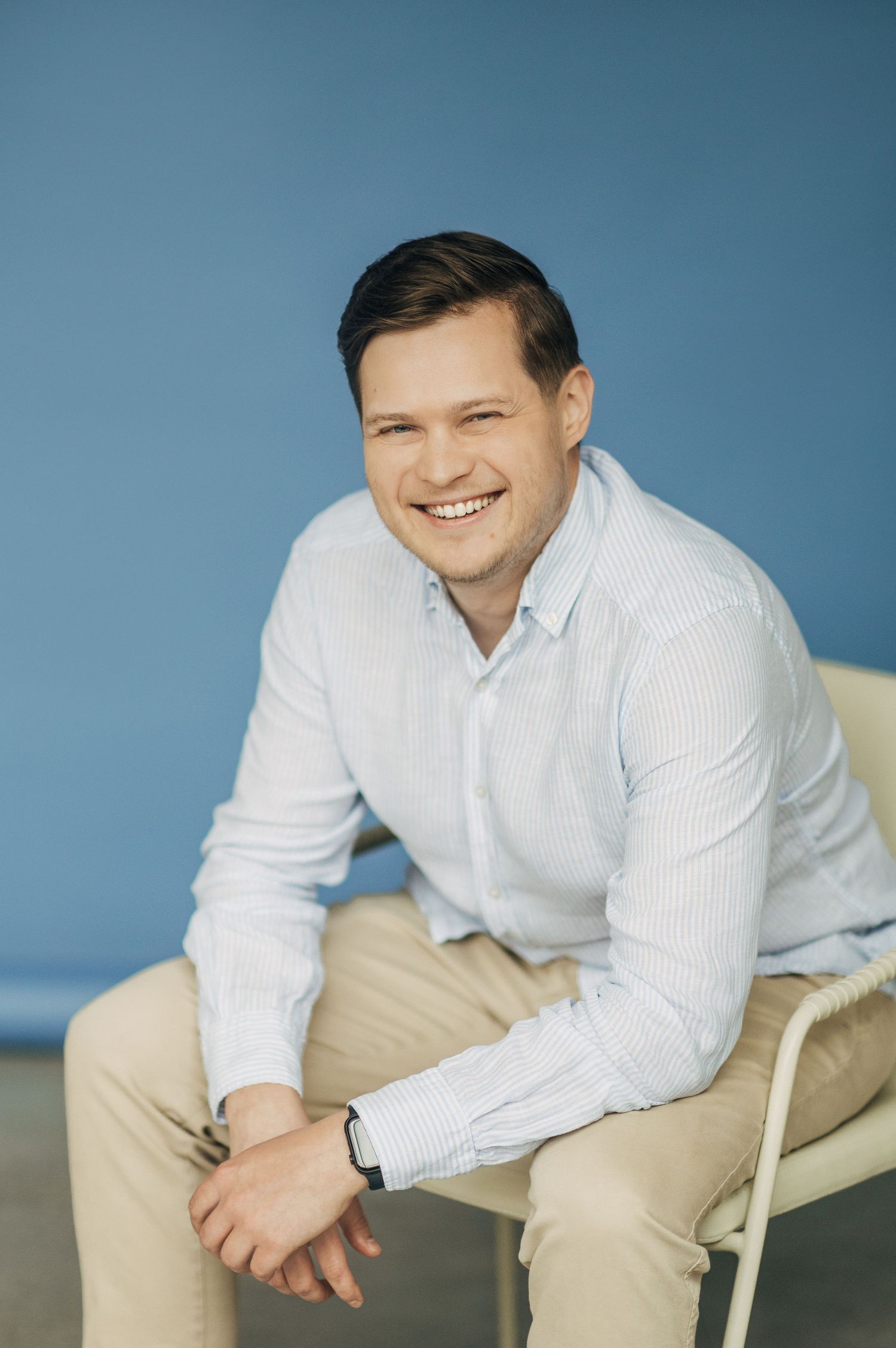 Casual portrait in white button-down shirt against blue background.