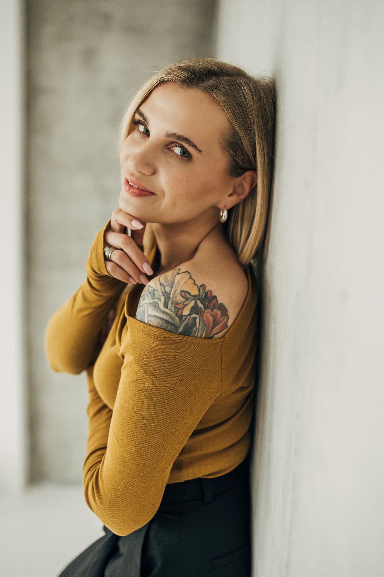 Studio portraits in mustard sweater showing artistic tattoo details.