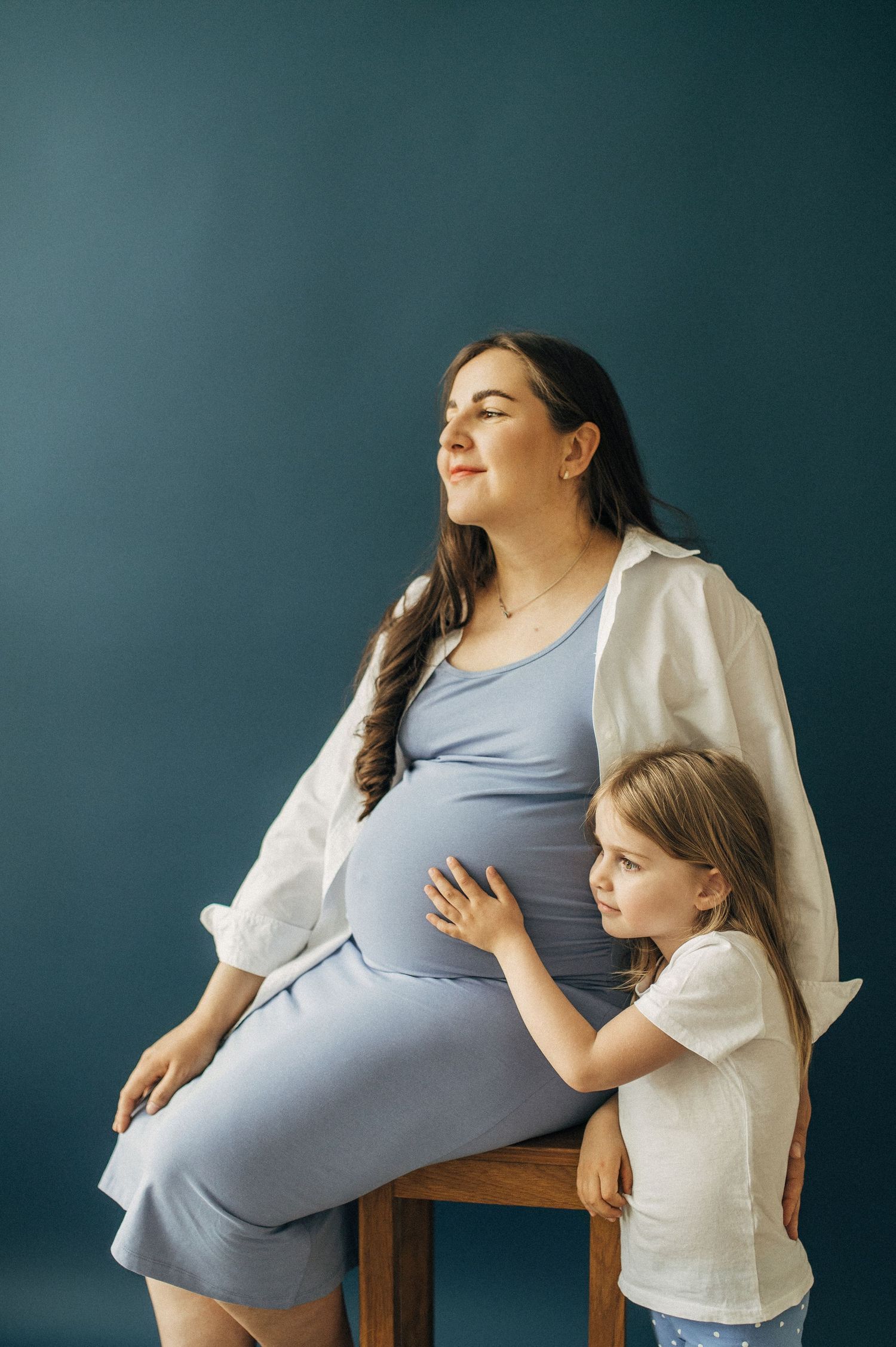 Maternity portrait against teal wall shows tender embrace.