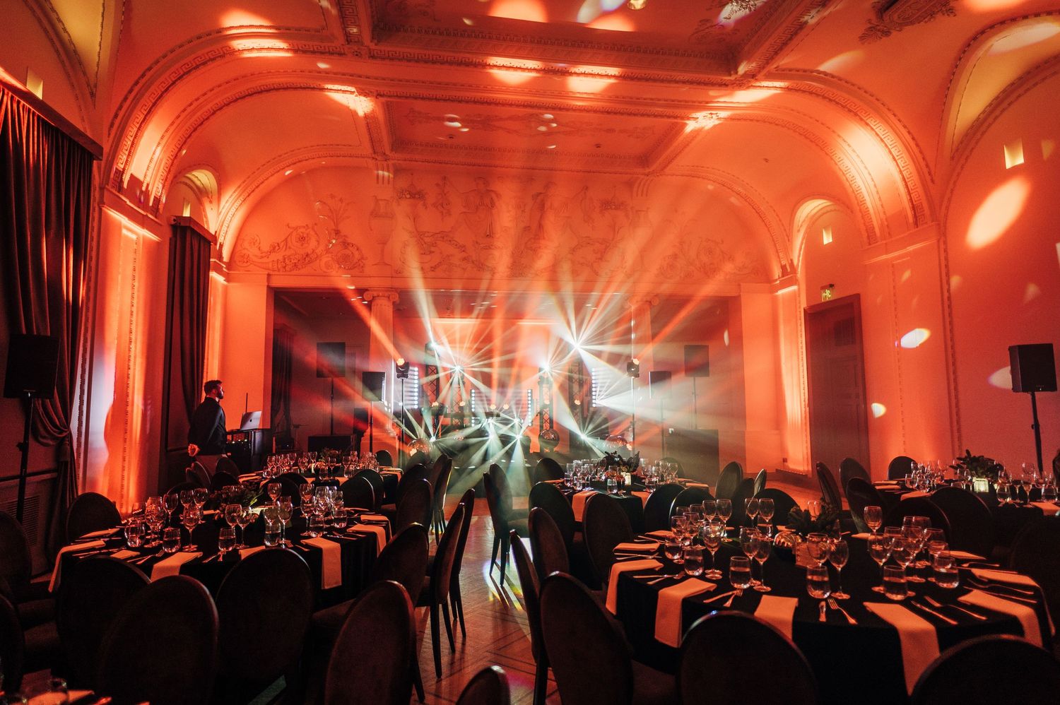 Large indoor venue with dramatic red lighting and silhouetted crowd creating an atmospheric ambiance.
