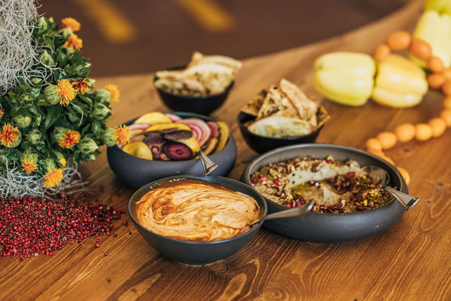 Rustic wooden table set with various bowls of colorful Indian dishes, spices, and garnishes in warm lighting.
