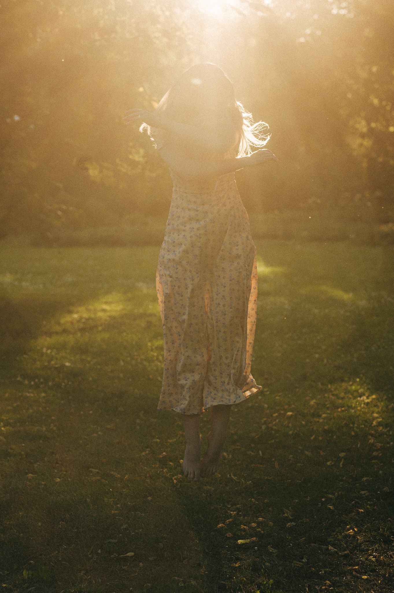 A dreamy backlit silhouette of a woman in a flowing dress standing in a sunlit meadow.