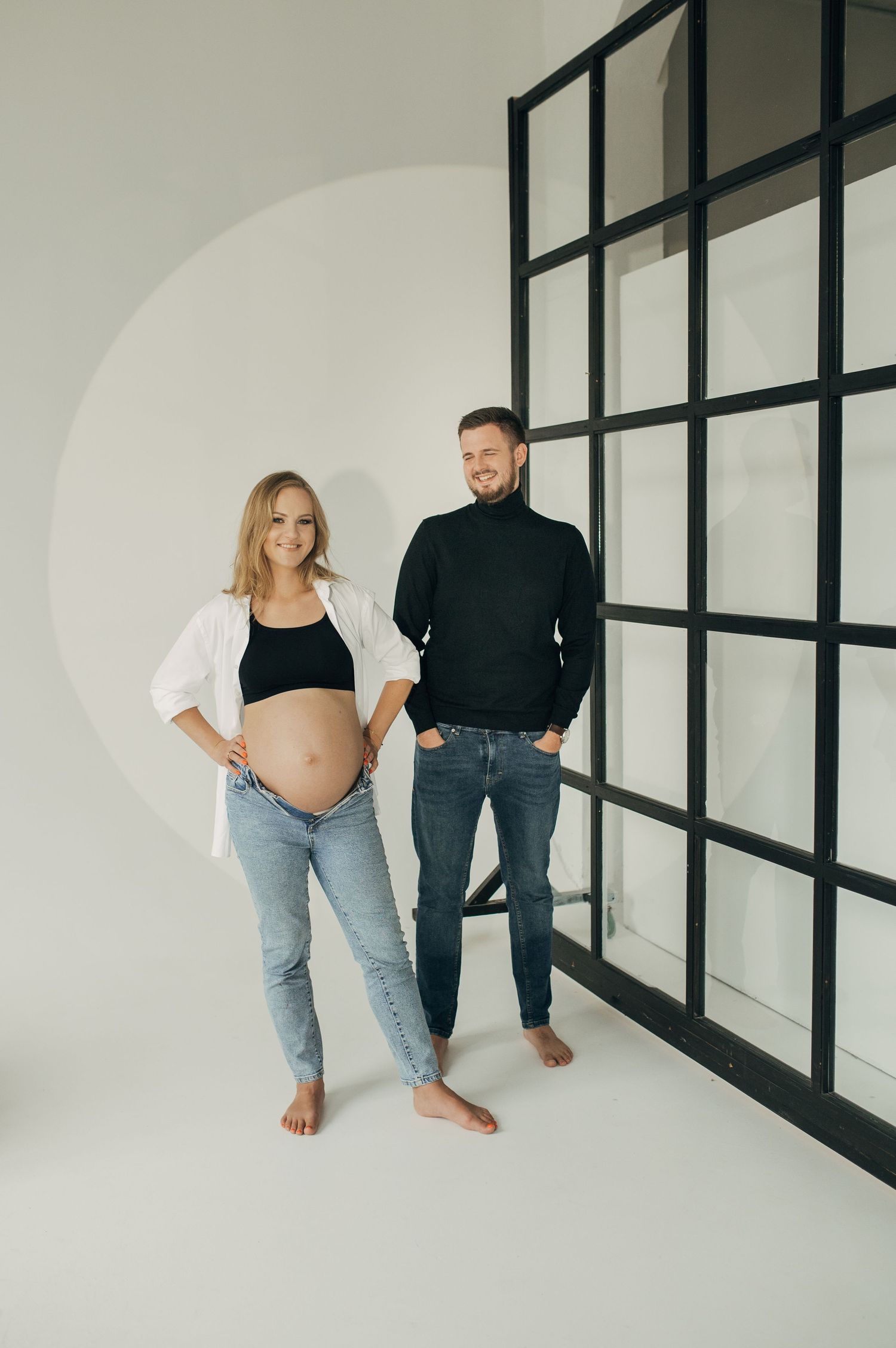 Modern minimalist maternity photos against white walls with black window frames.