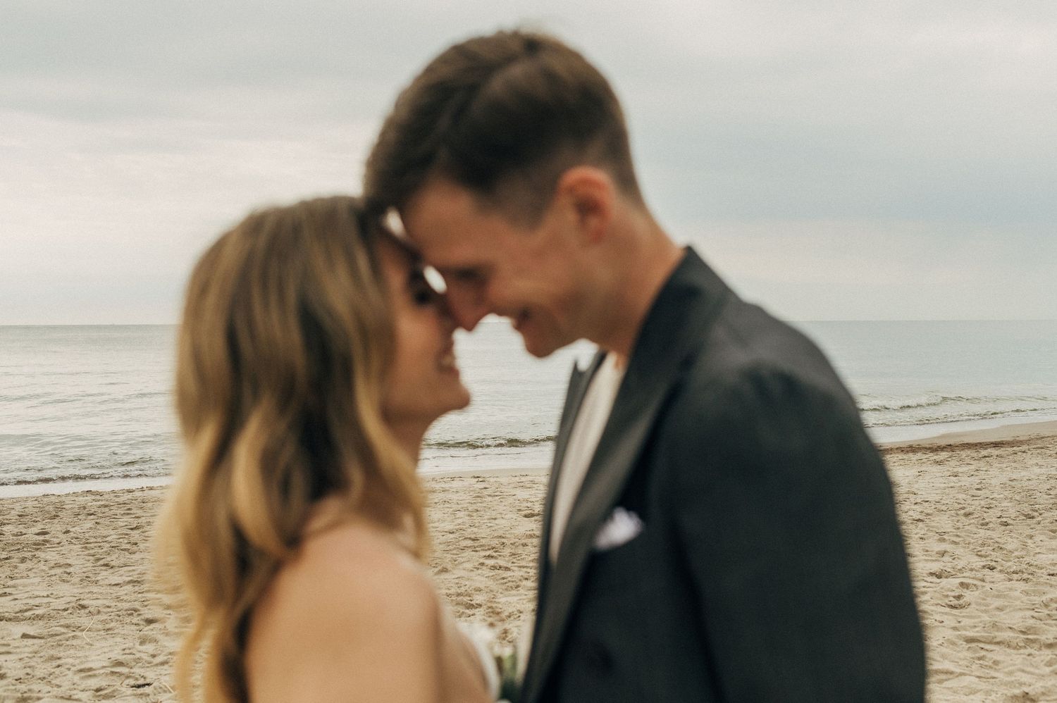 Romantic couple embraces on a cloudy beach during their wedding day.