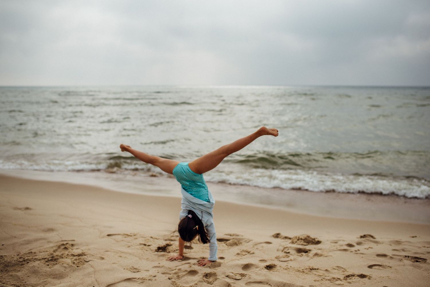 Kids playing and doing cartwheels on a sandy beach at sunset.
