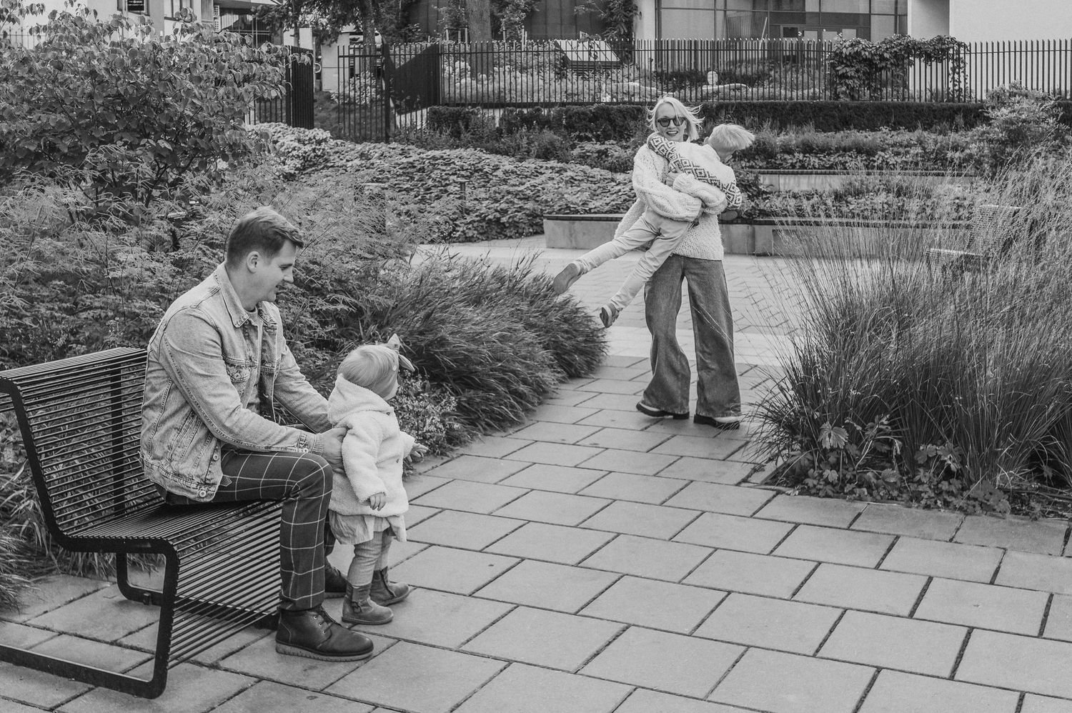 Black and white sequence showing playful family interactions on an outdoor stone patio.