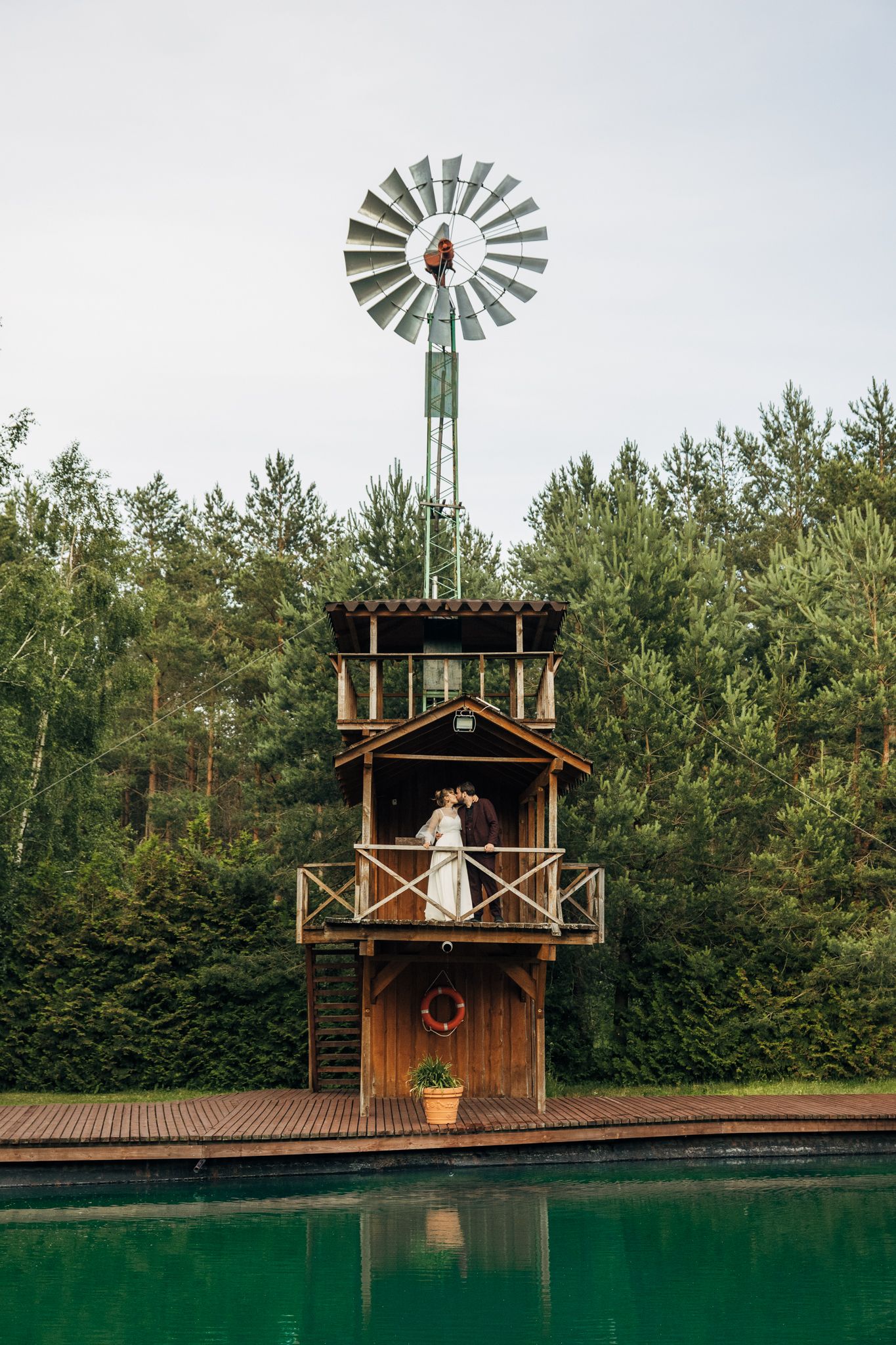 Rustic wooden platform with windmill backdrop next to reflective pond.