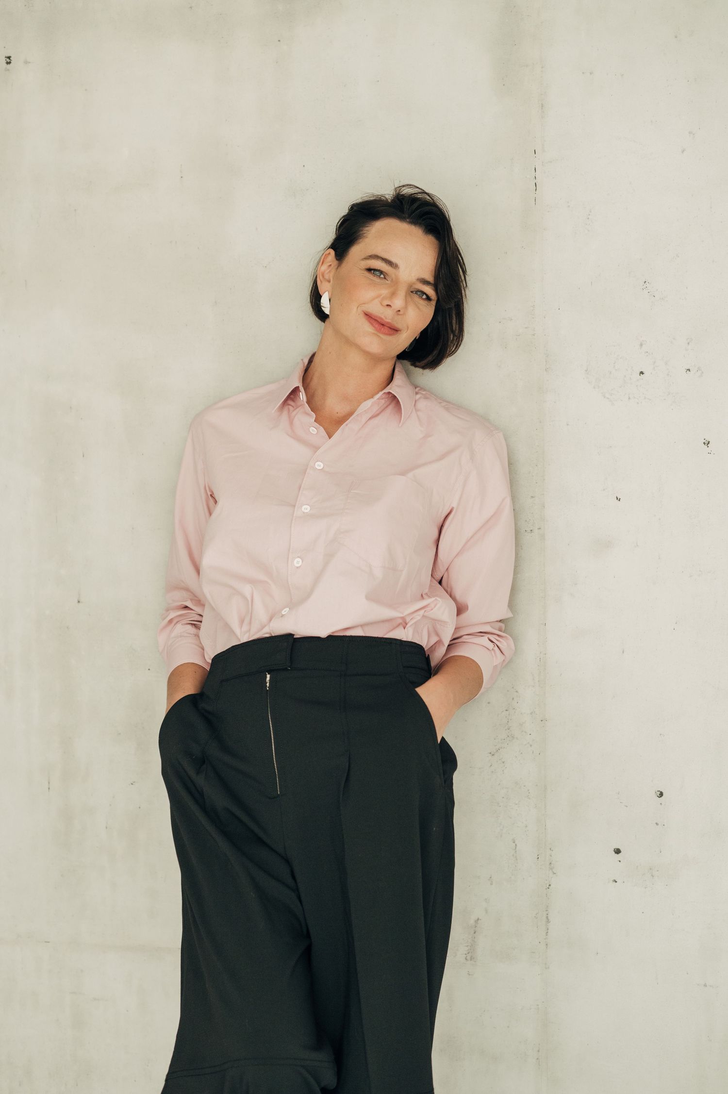 Professional fashion photo series showing a pink button-up shirt paired with black high-waisted pants against white wall.