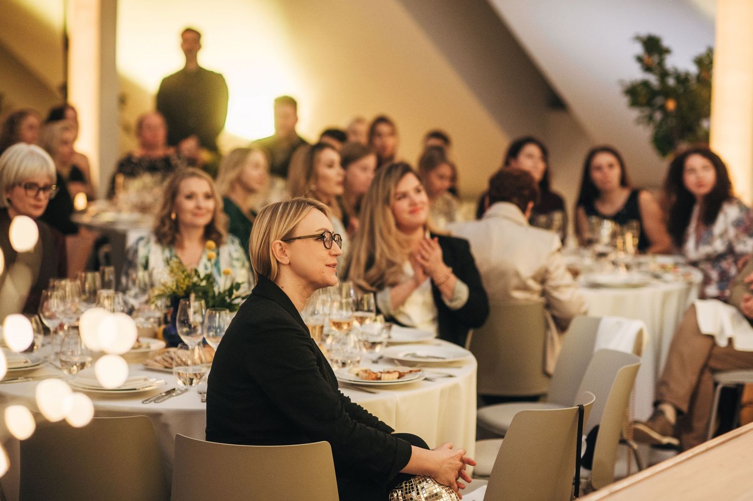 Guests seated at elegant round tables during an evening wedding reception with soft lighting and floral centerpieces.
