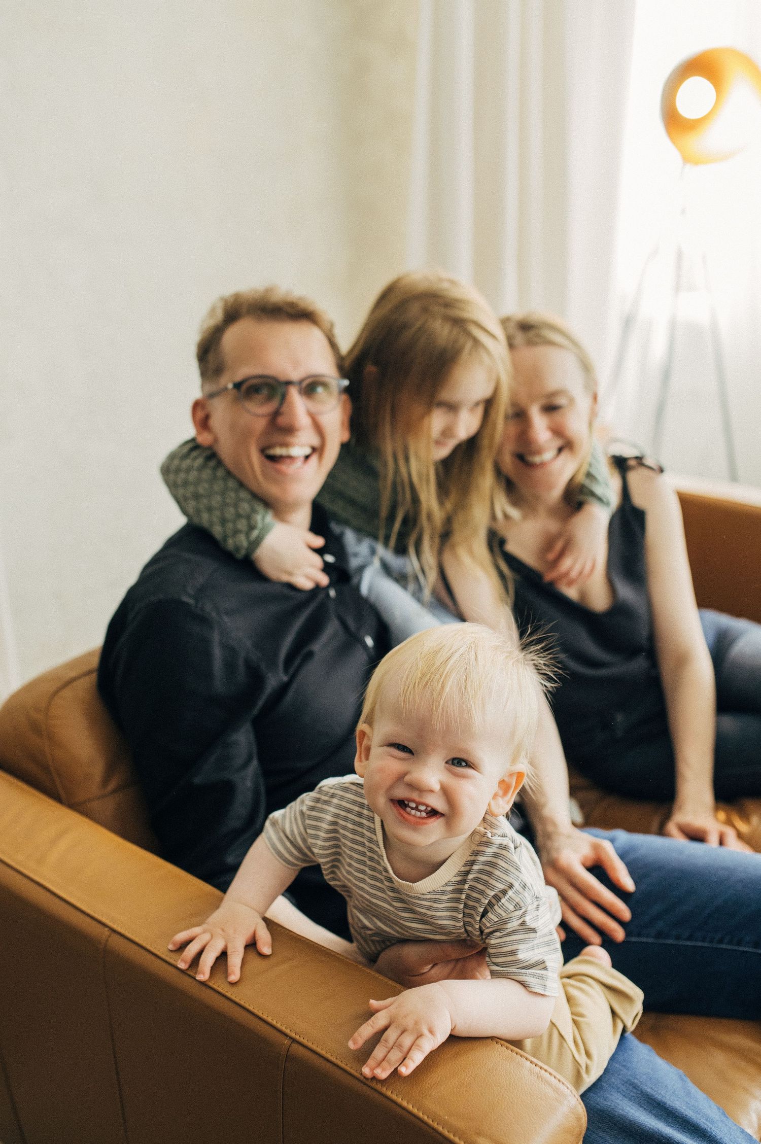 A joyful family moment on a brown leather couch with a laughing toddler in the foreground.