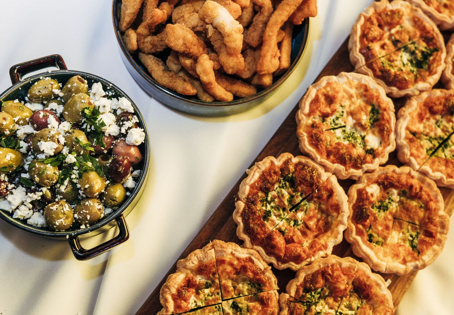 Assorted dishes including chicken wings, salads, pizzas and appetizers arranged on a white restaurant table.