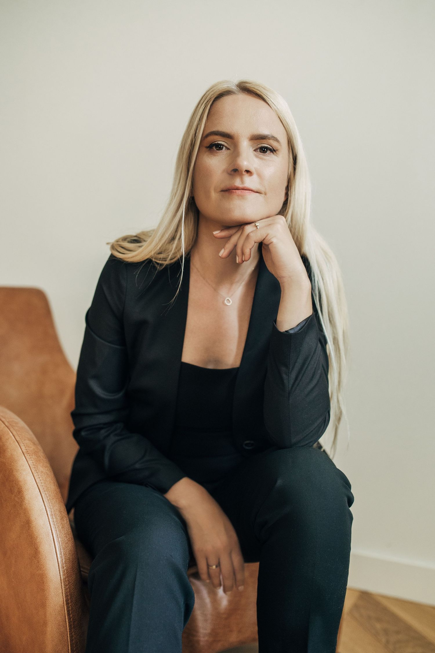 Professional sitting on a brown leather chair in a black business suit.