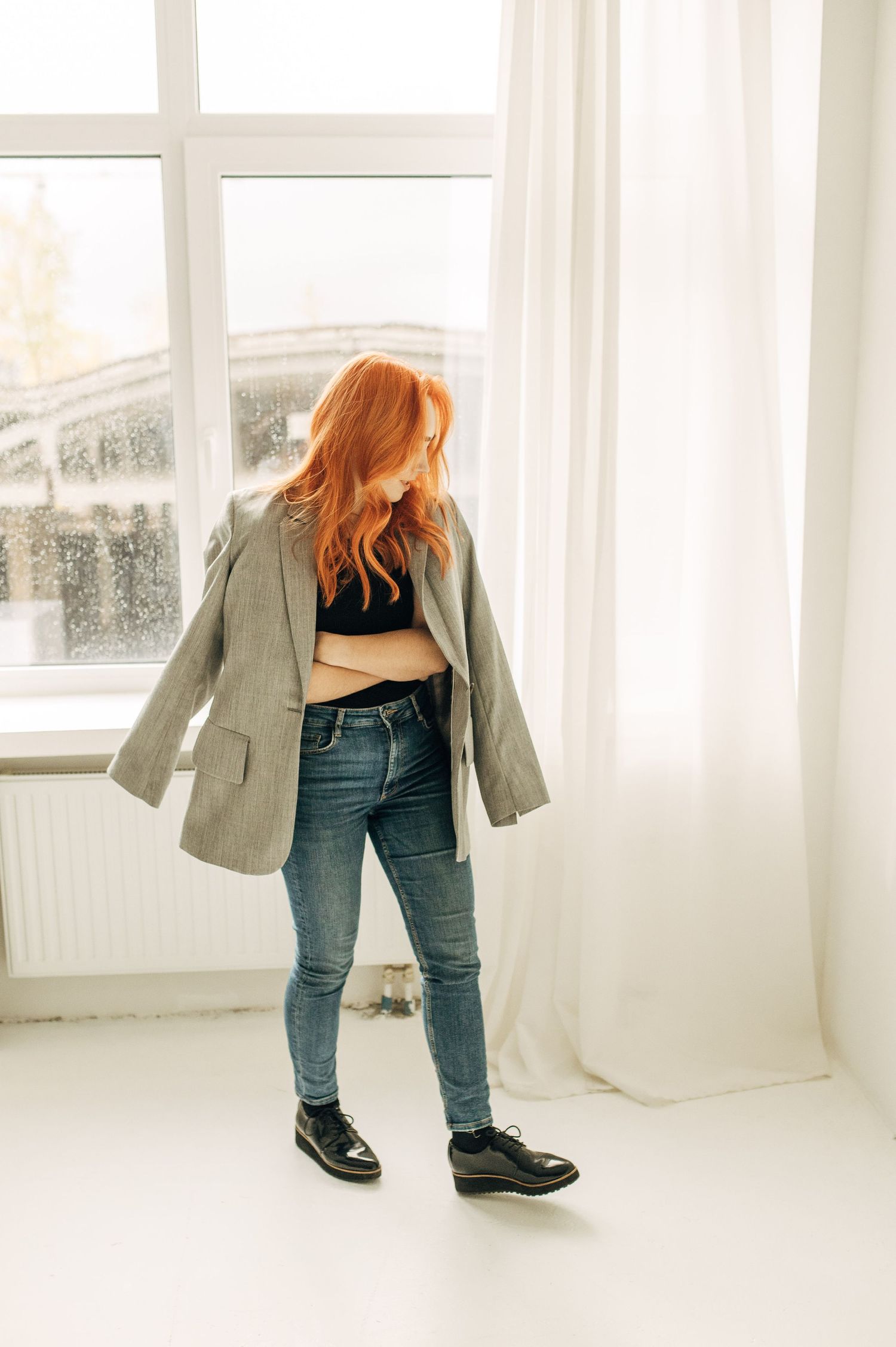 Fashion photo showing legs and torso in jeans and gray blazer against white background.