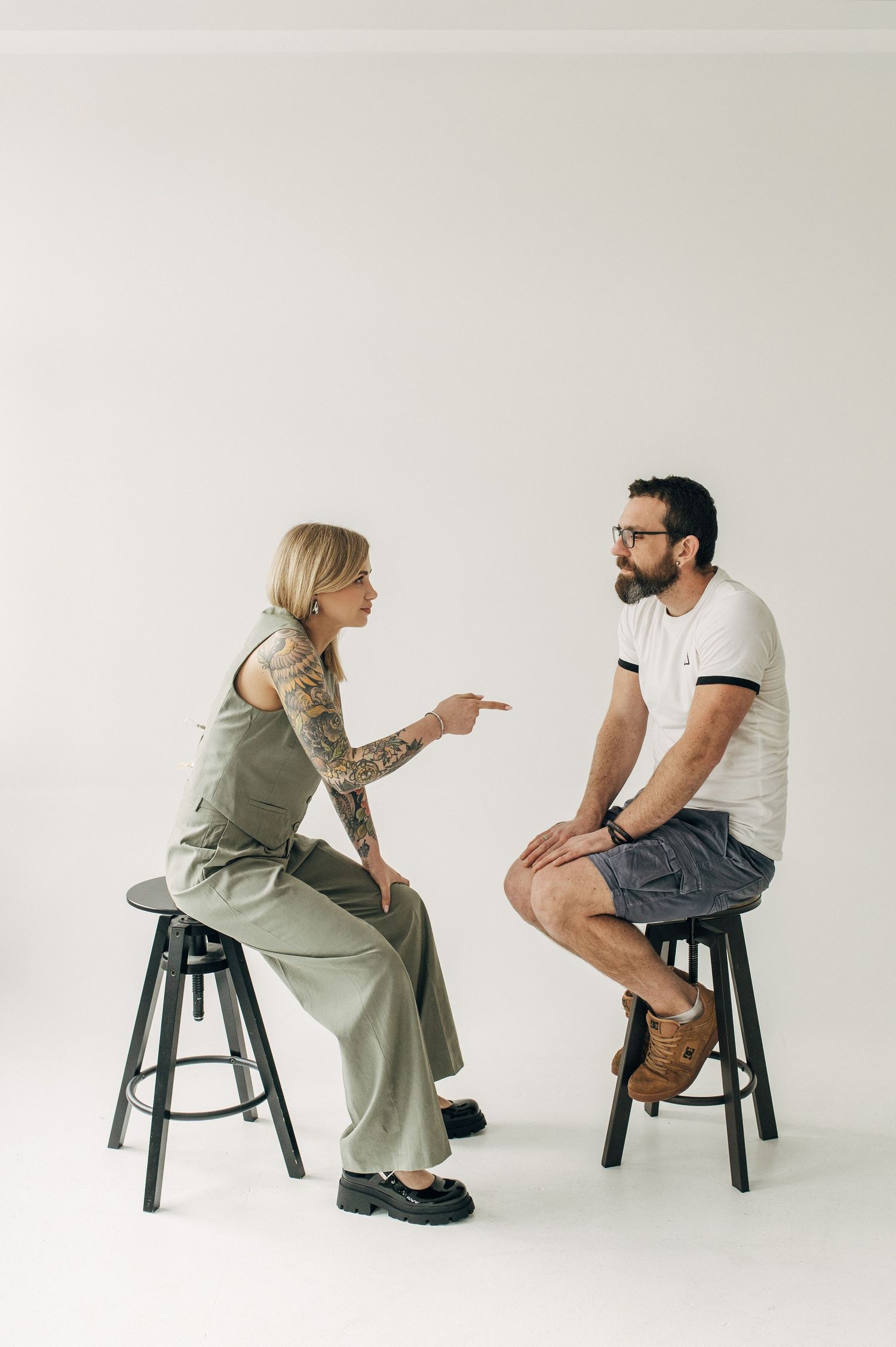 Two people having an expressive discussion while seated on dark stools in a studio setting.