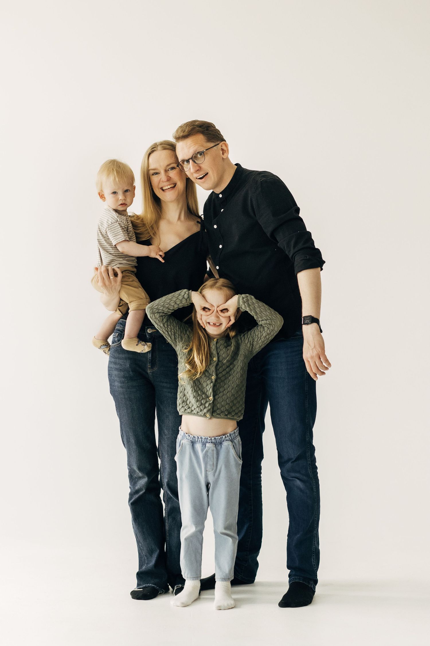 Family playfully posing together against a white studio backdrop in casual attire.