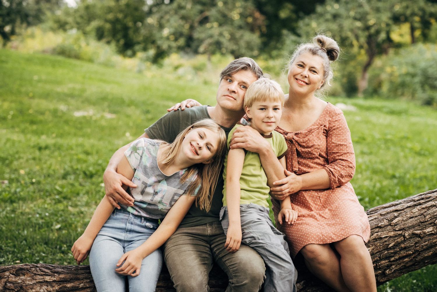 Candid outdoor family moments captured on a fallen log in a sunlit meadow.