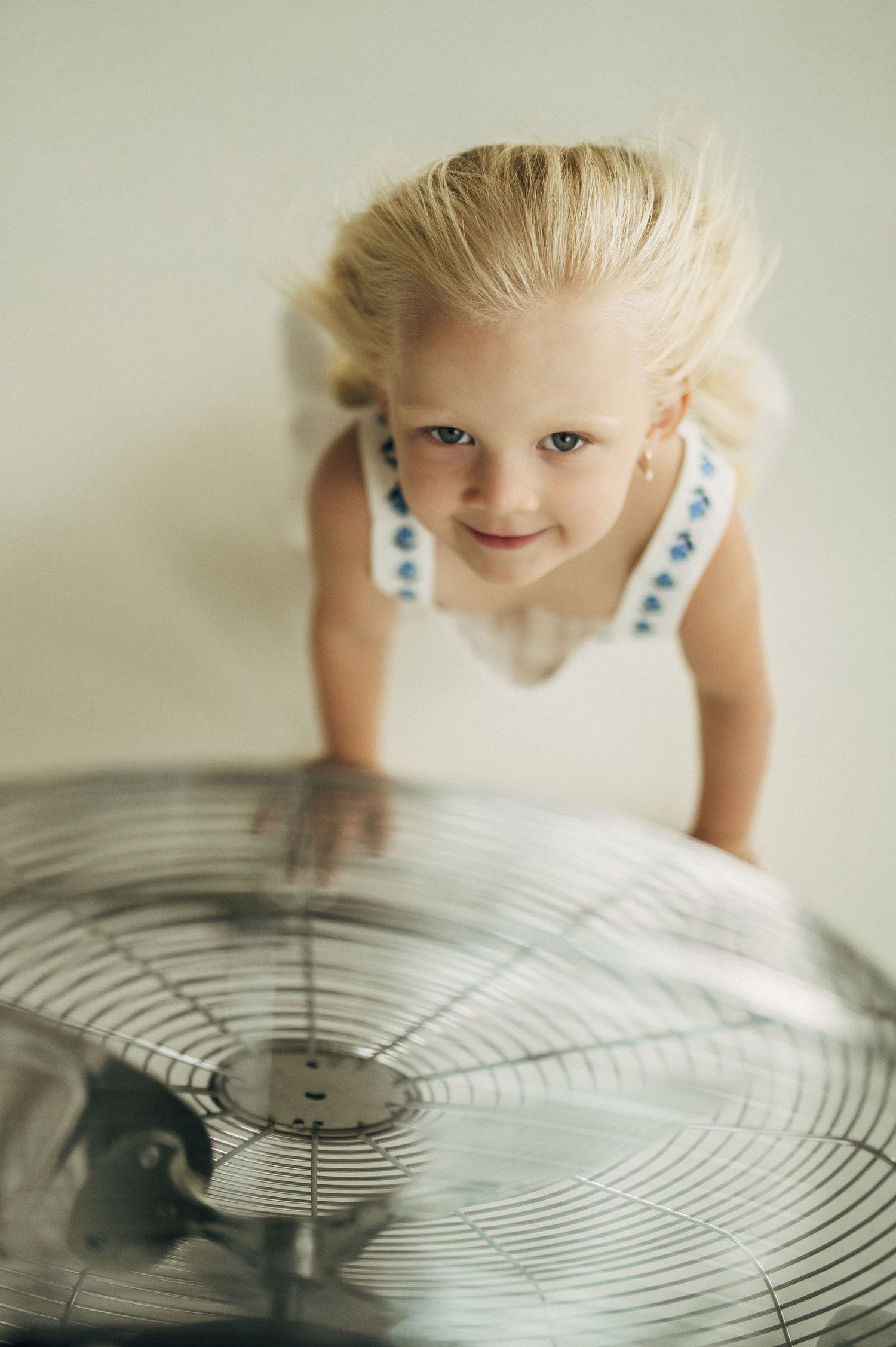 A child in a white dress leans over a large vintage fan, creating a soft and dreamy portrait.