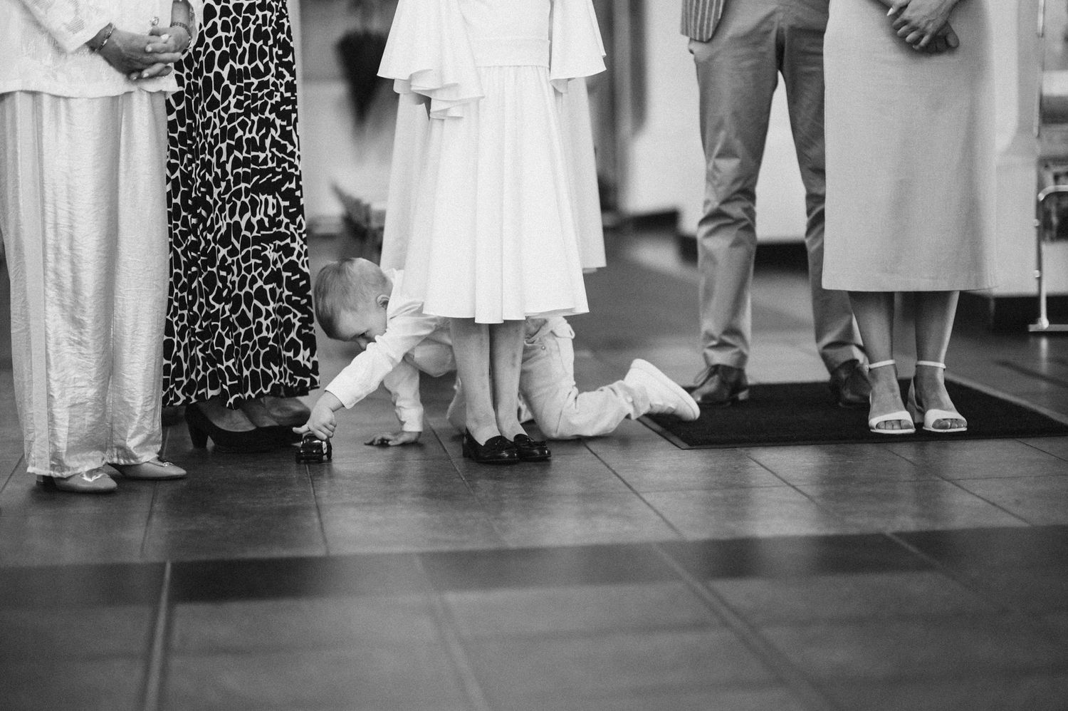 Black and white photo of children and adults feet standing together at a formal indoor event.