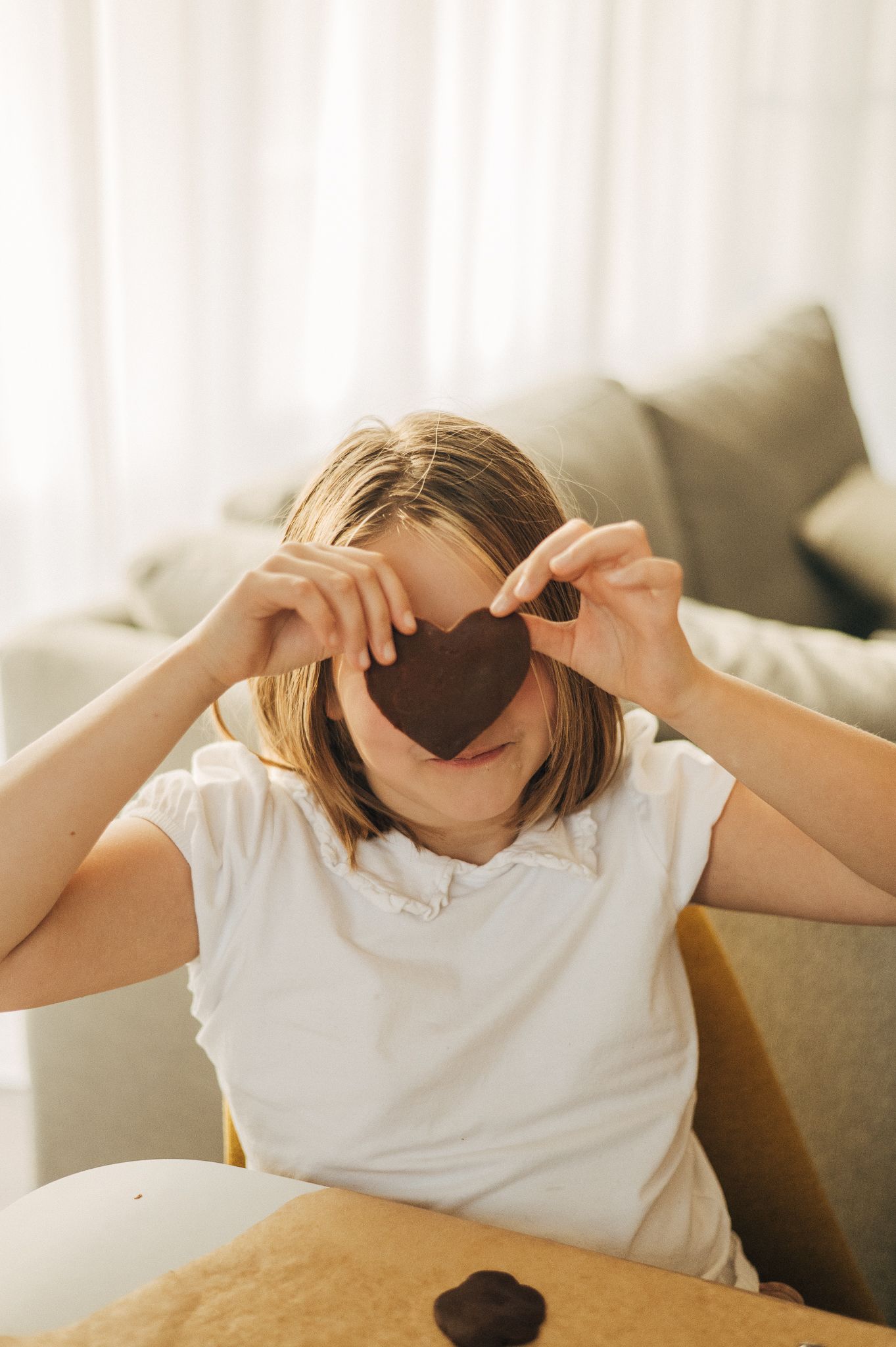 Person in white t-shirt making heart shapes with hands in bright sunlit room.